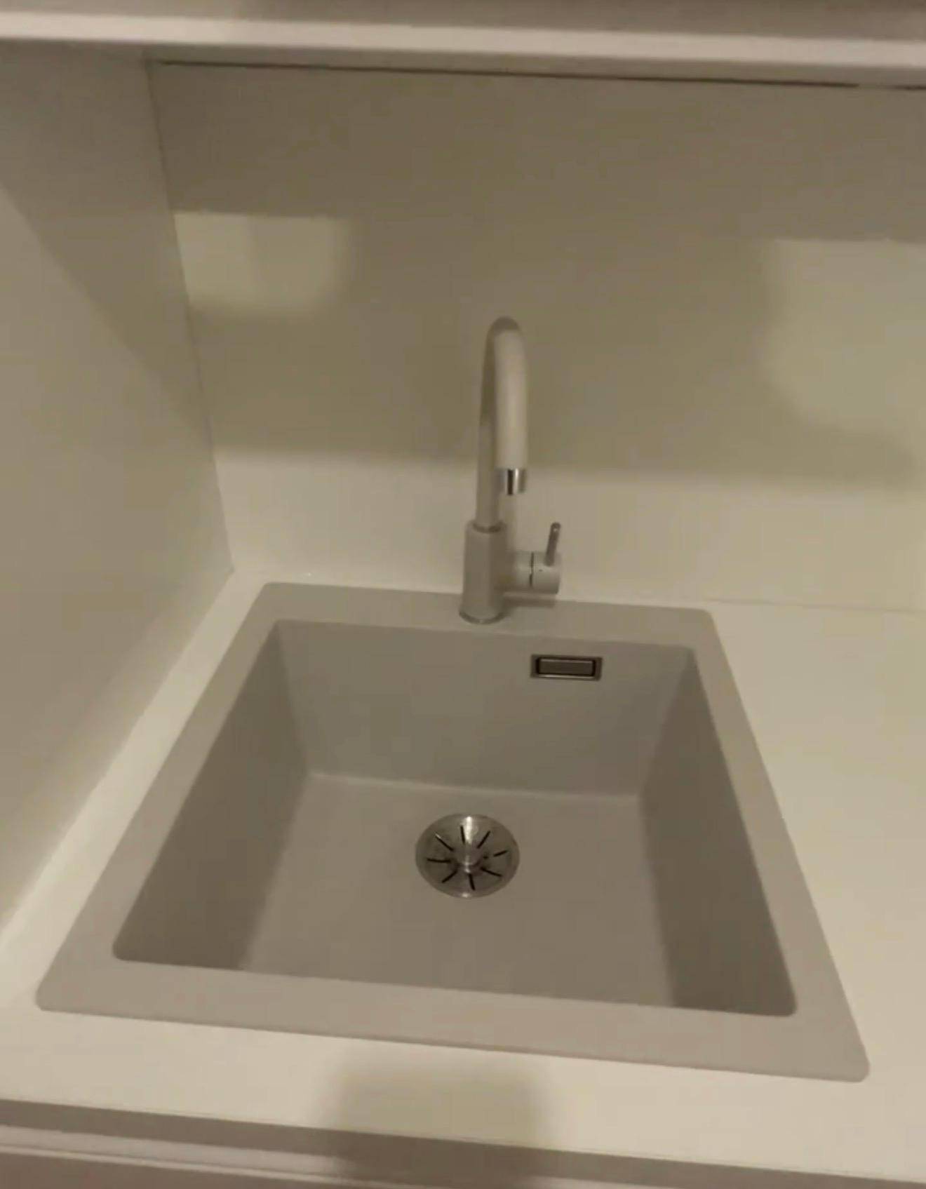 Detailaufnahme der modernen Küchenspüle mit weißem Wasserhahn und Spülbecken in der Einbauküche.