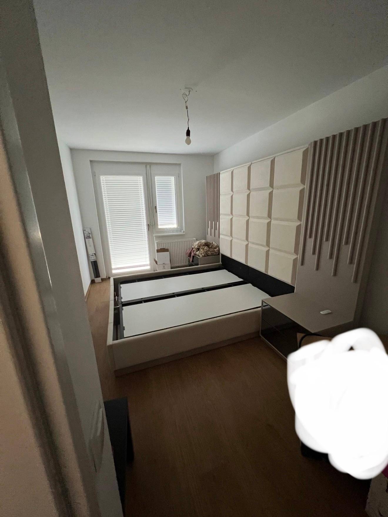 Schlafzimmer mit modernem Bettgestell, Holzboden und Fenster mit Jalousien für Privatsphäre.