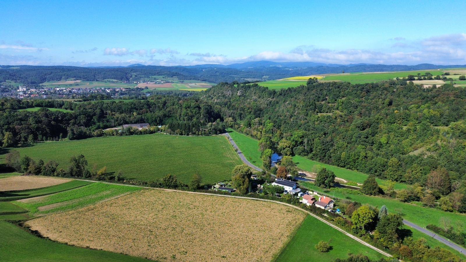 Panoramablick über eine weite, hügelige Landschaft mit Feldern, Wäldern und einem Dorf am Horizont.