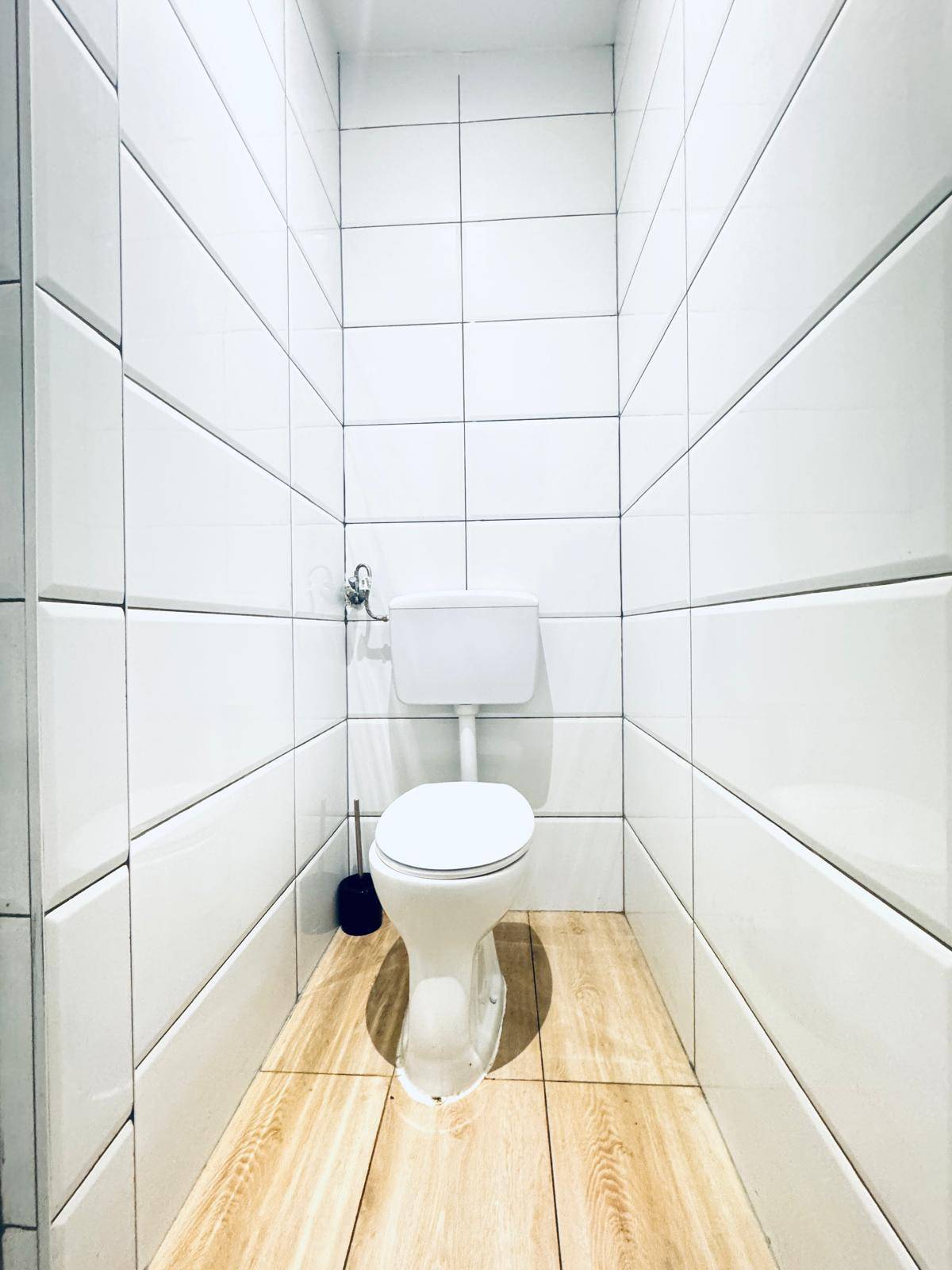 Schlichtes WC mit weißen Fliesen an den Wänden und Laminatboden.
