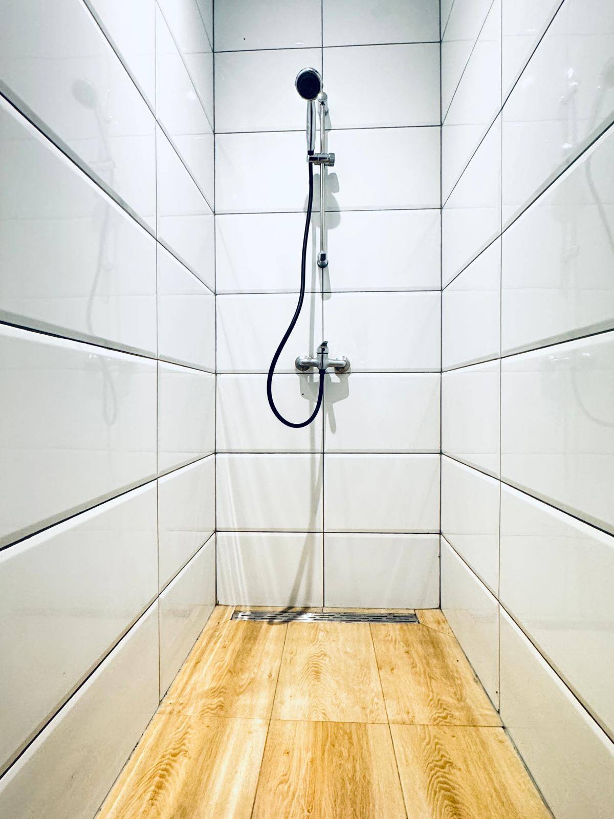Duschbereich mit weißen Wandfliesen und Laminatboden in einem modernen Badezimmer.