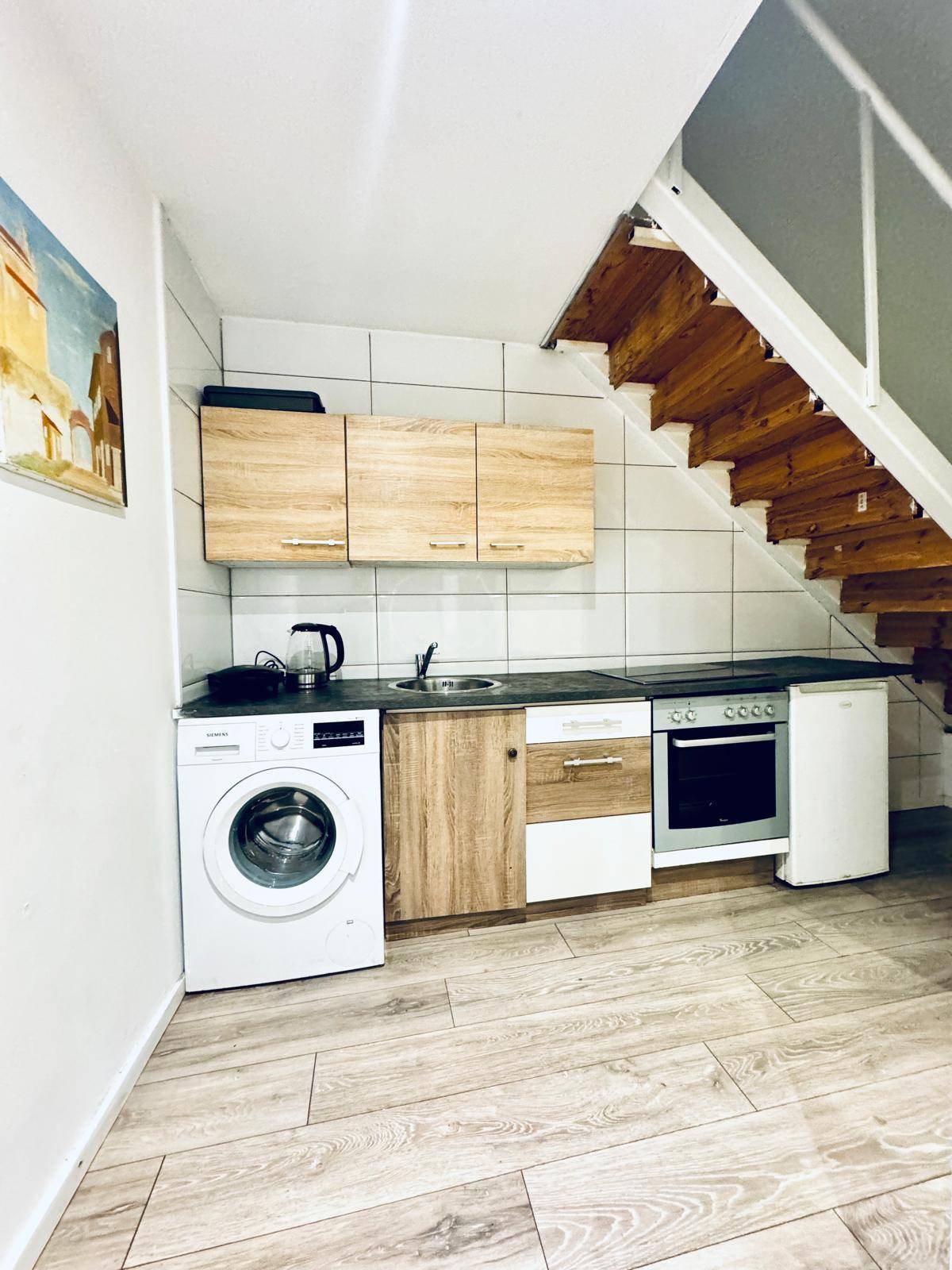 Kompakte Küchenzeile unter einer Treppe mit Waschmaschine, Ofen und Kühlschrank.