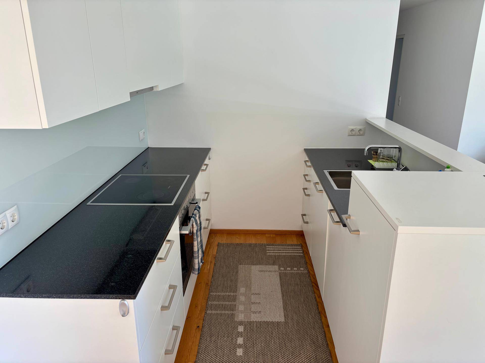 Moderne Küche mit weißen Schränken, schwarzen Arbeitsplatten und integriertem Kochfeld.