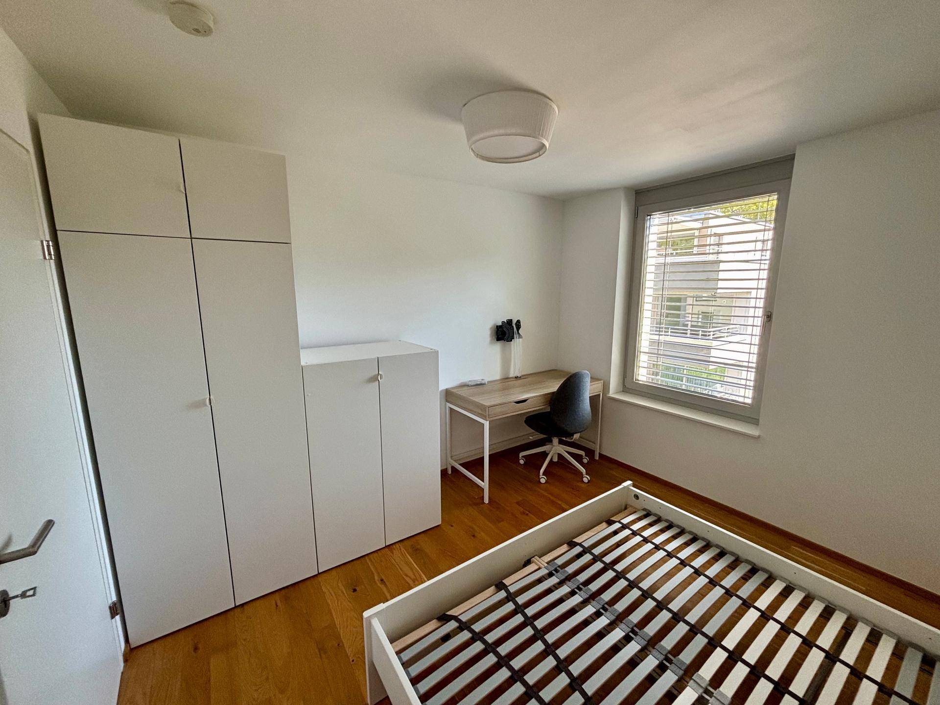 Helles Schlafzimmer mit Holzboden, Schreibtisch und weißem Kleiderschrank, ideal für Gäste.