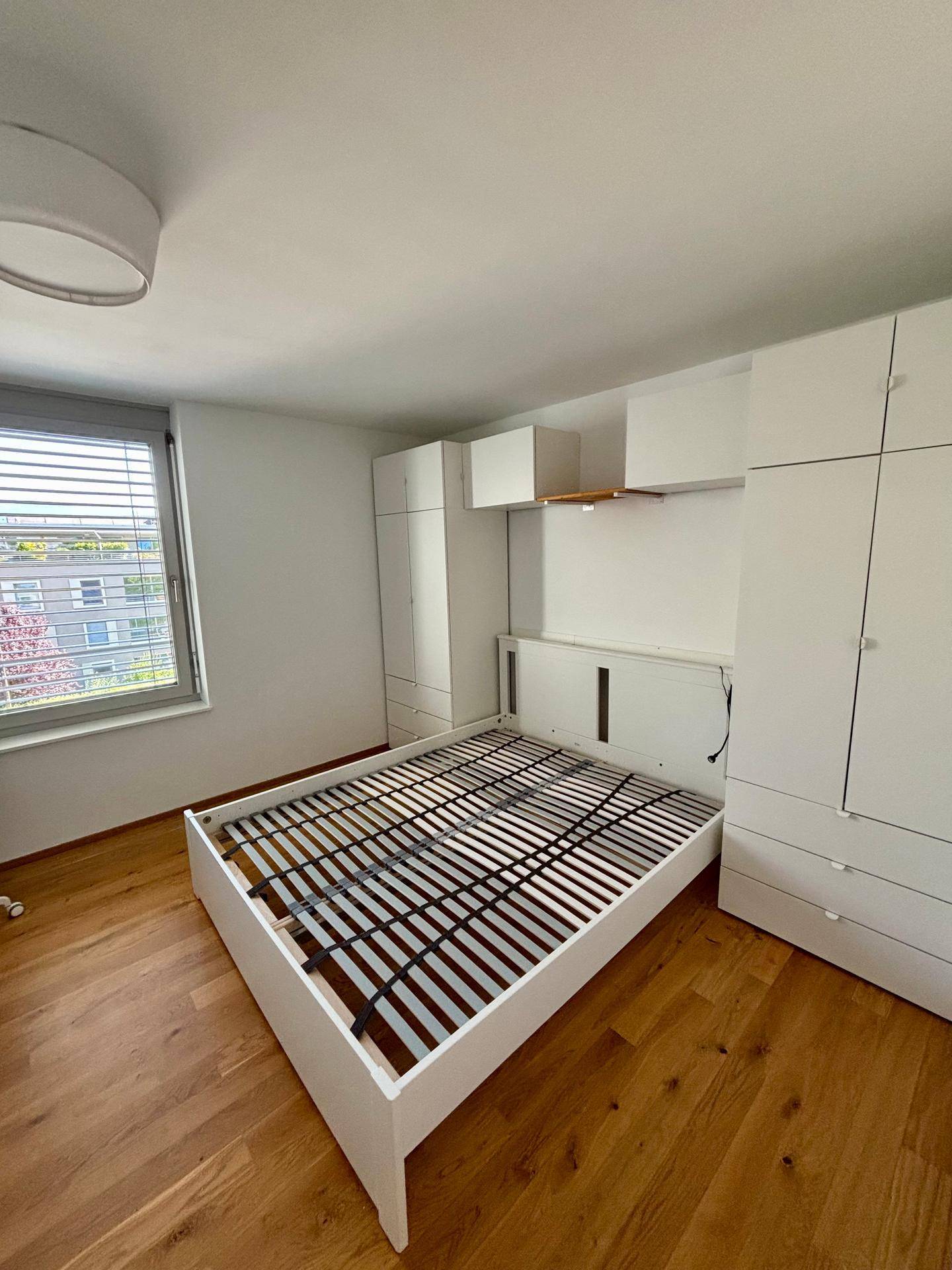Schlafzimmer mit Holzboden, Fenster und weißen Einbauschränken, bereit für die Einrichtung.