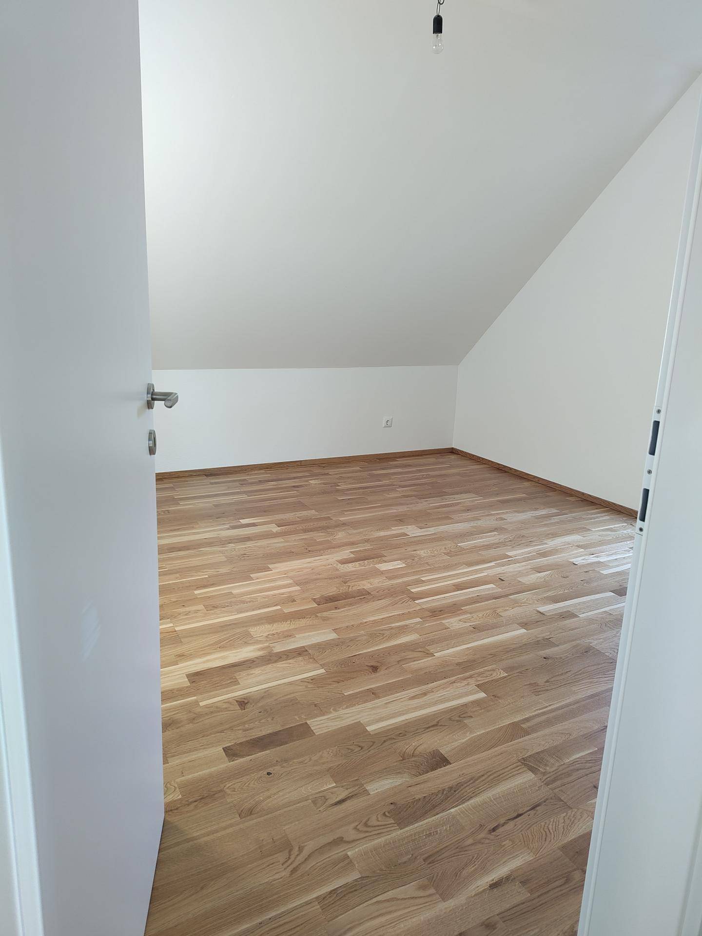 Geräumiges Zimmer mit Holzboden und Dachschräge, ideal als Schlaf- oder Kinderzimmer nutzbar.