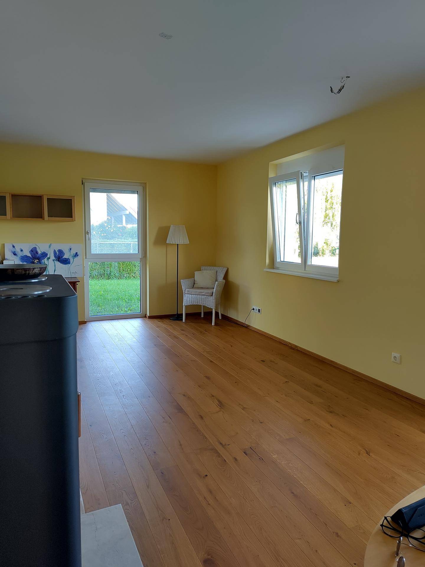 Heller Wohnbereich mit gelben Wänden, Holzboden und Zugang zum Garten, inklusive Kaminofen.