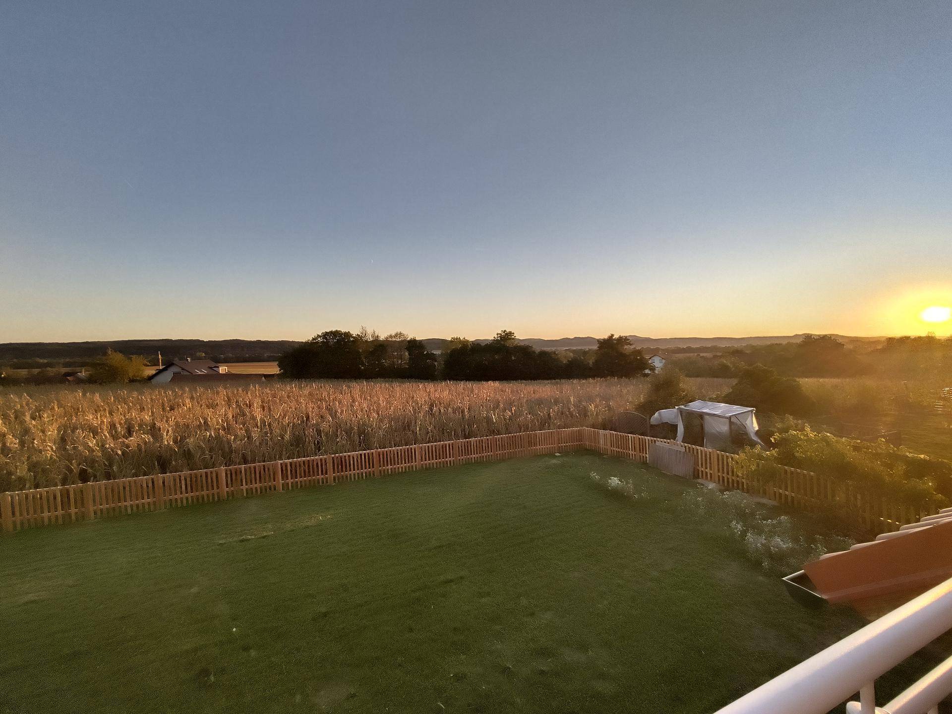 Großer Garten mit Rasenfläche und weitem Blick über Felder und die ländliche Umgebung bei Sonnenuntergang.