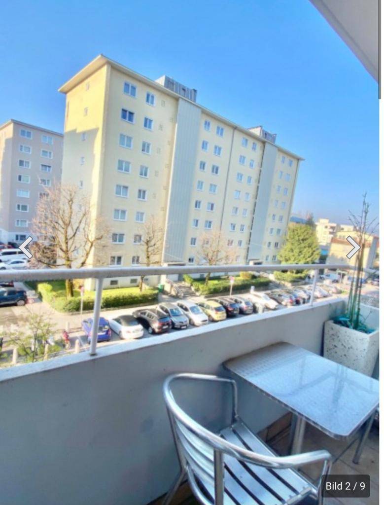 Balkon mit Sitzgelegenheiten und Blick auf umliegende Wohngebäude und Parkplätze.