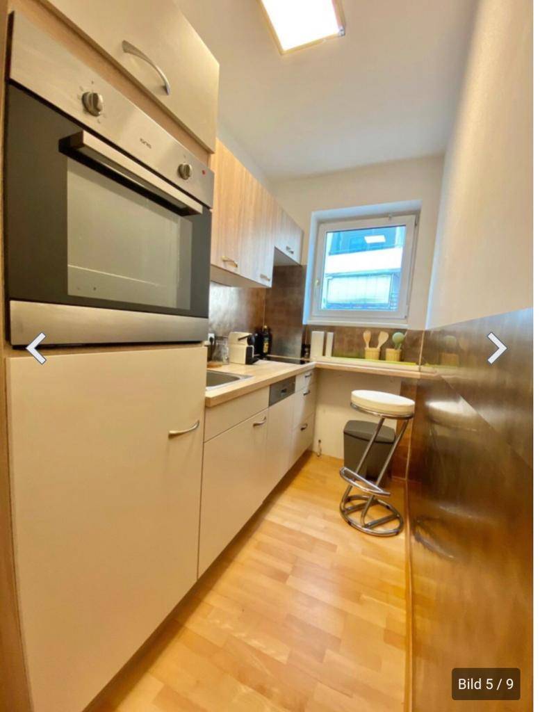 Schmale Küche mit Einbauofen, Holzschränken und Fenster für natürliches Licht.