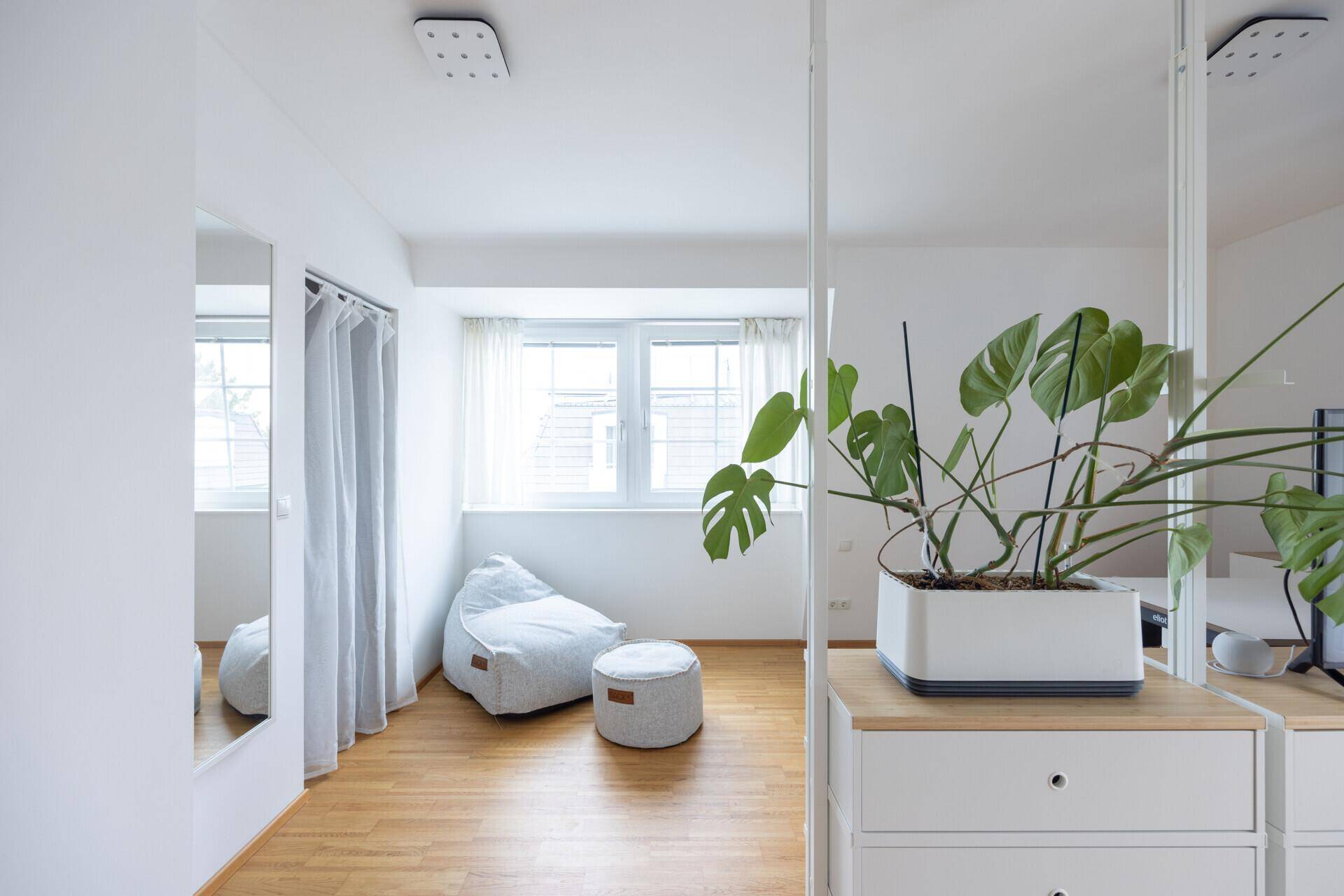 Helles Schlafzimmer mit Holzfußboden, großen Fenstern und praktischen Spiegelschränken.