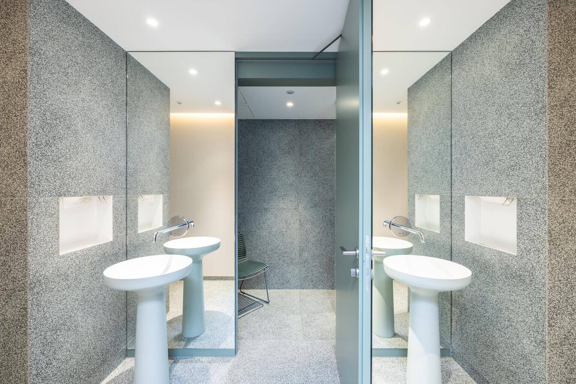 Modernes Badezimmer mit zwei freistehenden Waschbecken, großen Spiegeln und grauen Fliesenwänden.