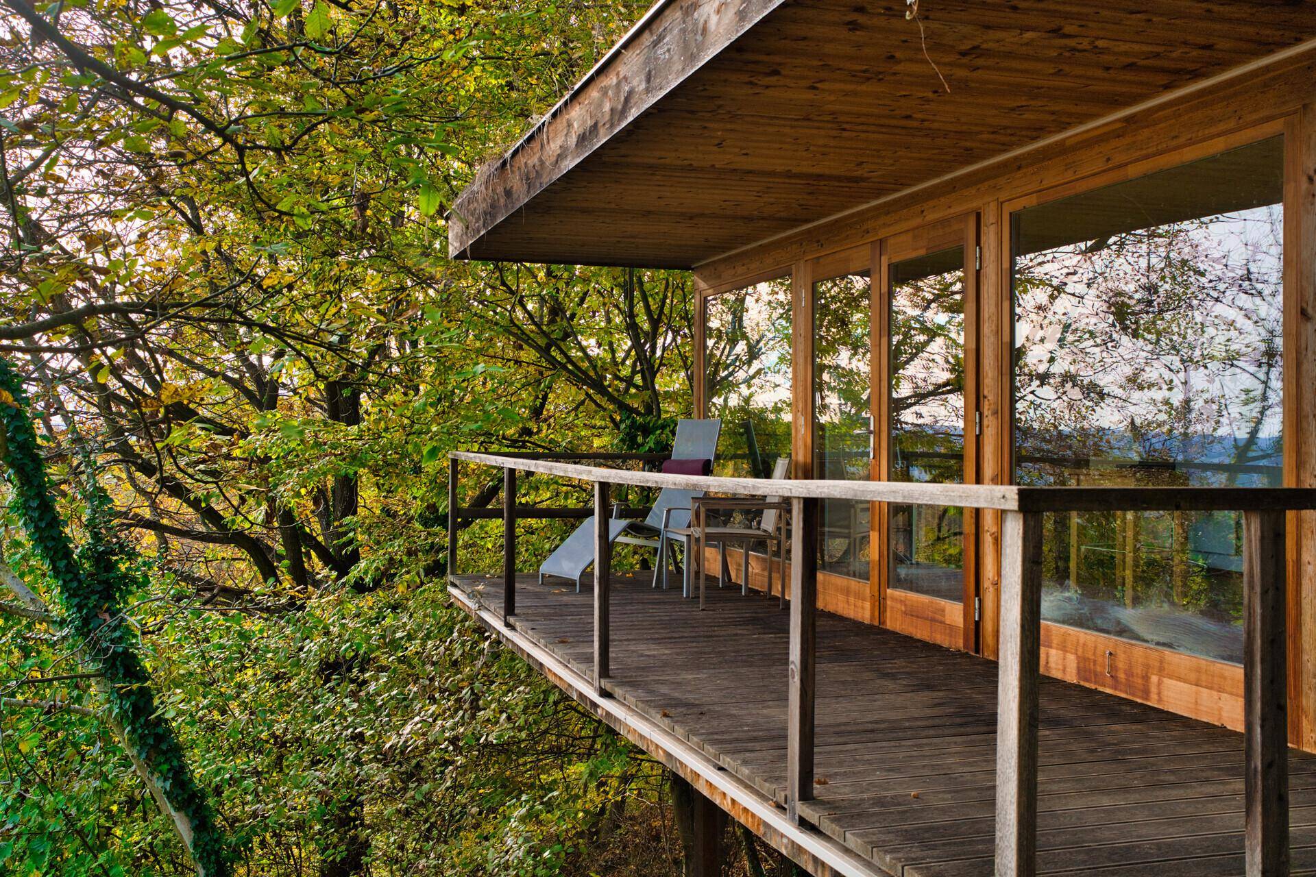 Holzbalkon mit Sitzgelegenheiten und weitem Blick in die grüne Baumlandschaft.