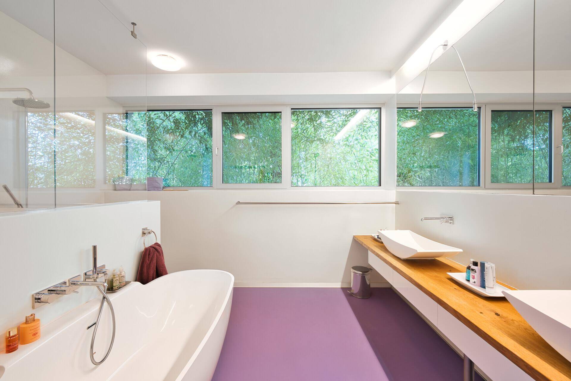 Modernes Badezimmer mit freistehender Badewanne, Doppelwaschbecken und großen Fenstern mit Blick ins Grüne.