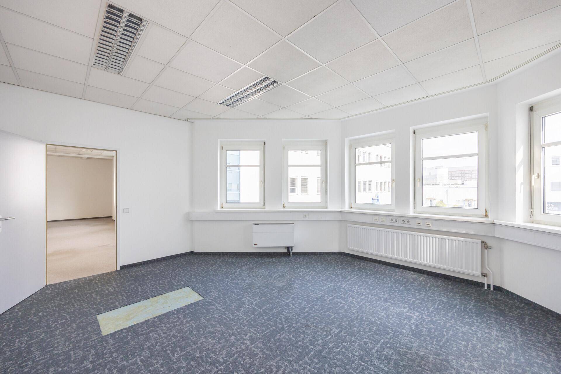 Eckbüro mit Teppichboden, mehreren Fenstern und Heizkörpern, bietet viel natürliches Licht.