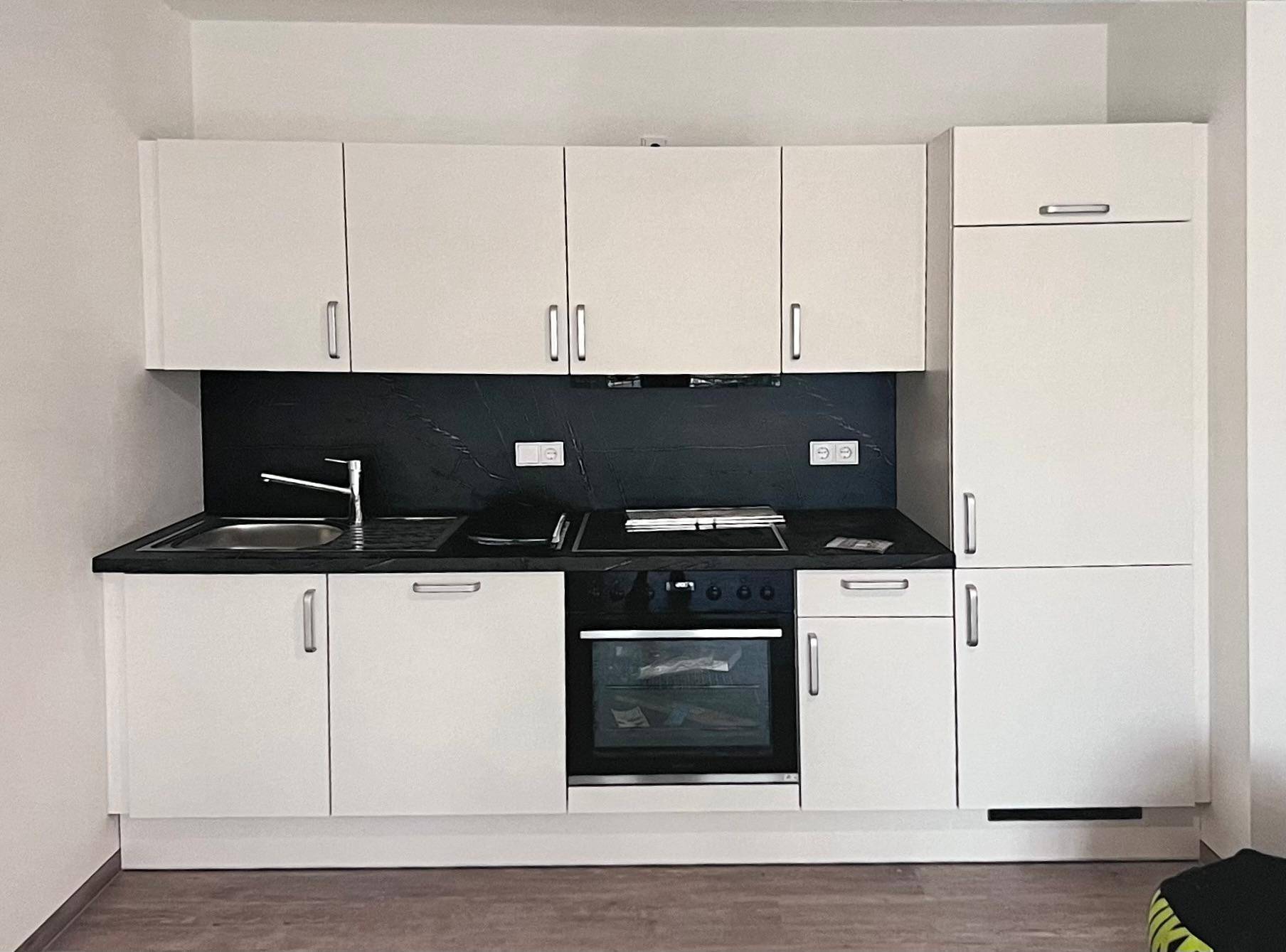 Moderne Einbauküche mit weißen Schränken, schwarzer Arbeitsplatte und integrierten Geräten.