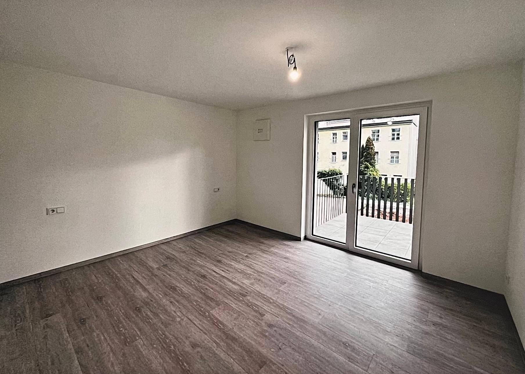 Geräumiger Raum mit Laminatboden und Zugang zu einem Balkon mit Blick ins Grüne.