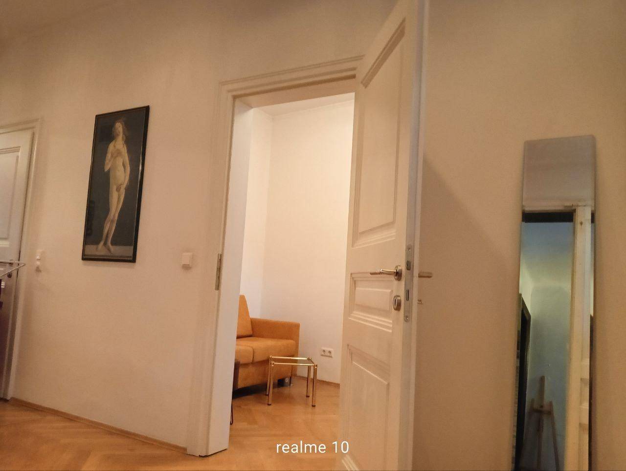 Heller Flur mit Parkettboden und offener Tür zu einem weiteren Zimmer.