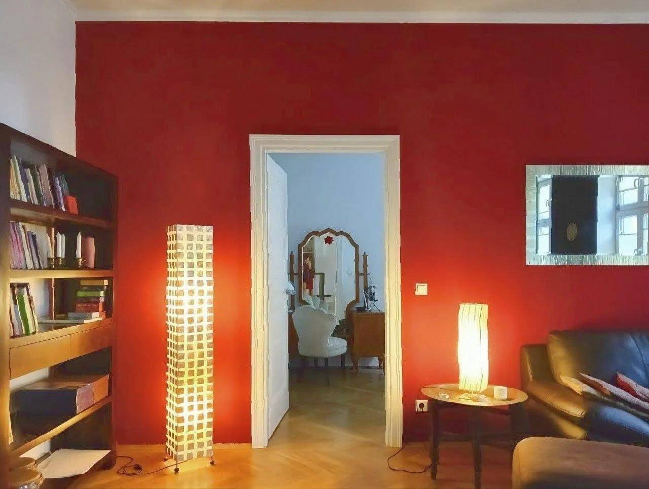 Wohnzimmer mit roter Akzentwand, Bücherregal und dekorativen Stehlampen.