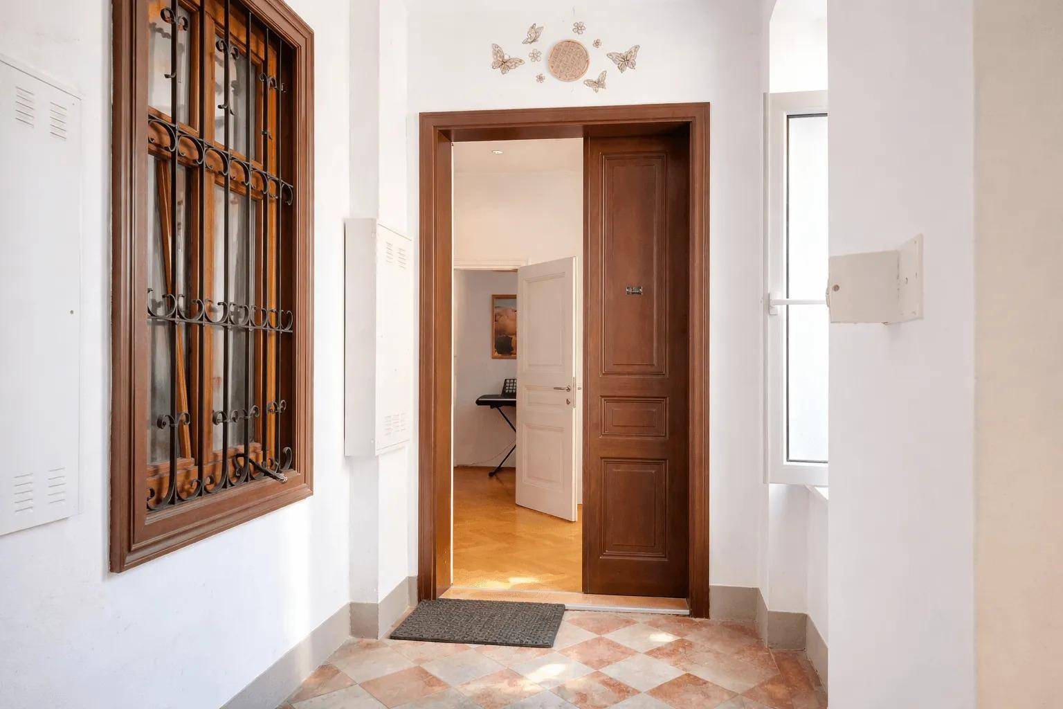 Eingangsbereich mit Holztür, Fenster mit Gitter und gemusterten Fliesenboden.