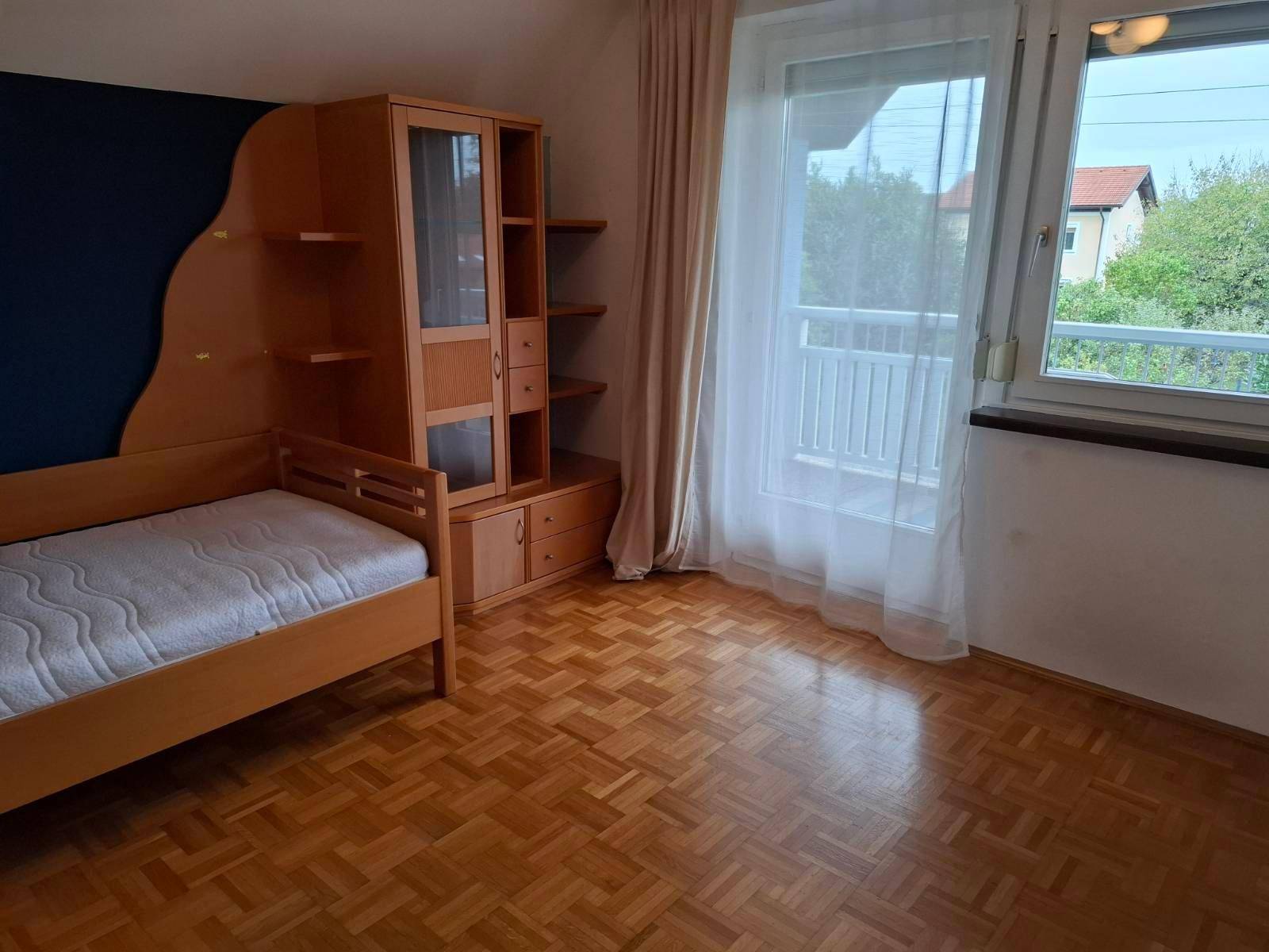 Kinderzimmer mit Einzelbett, Holzmöbeln, Parkettboden und Zugang zum Balkon.
