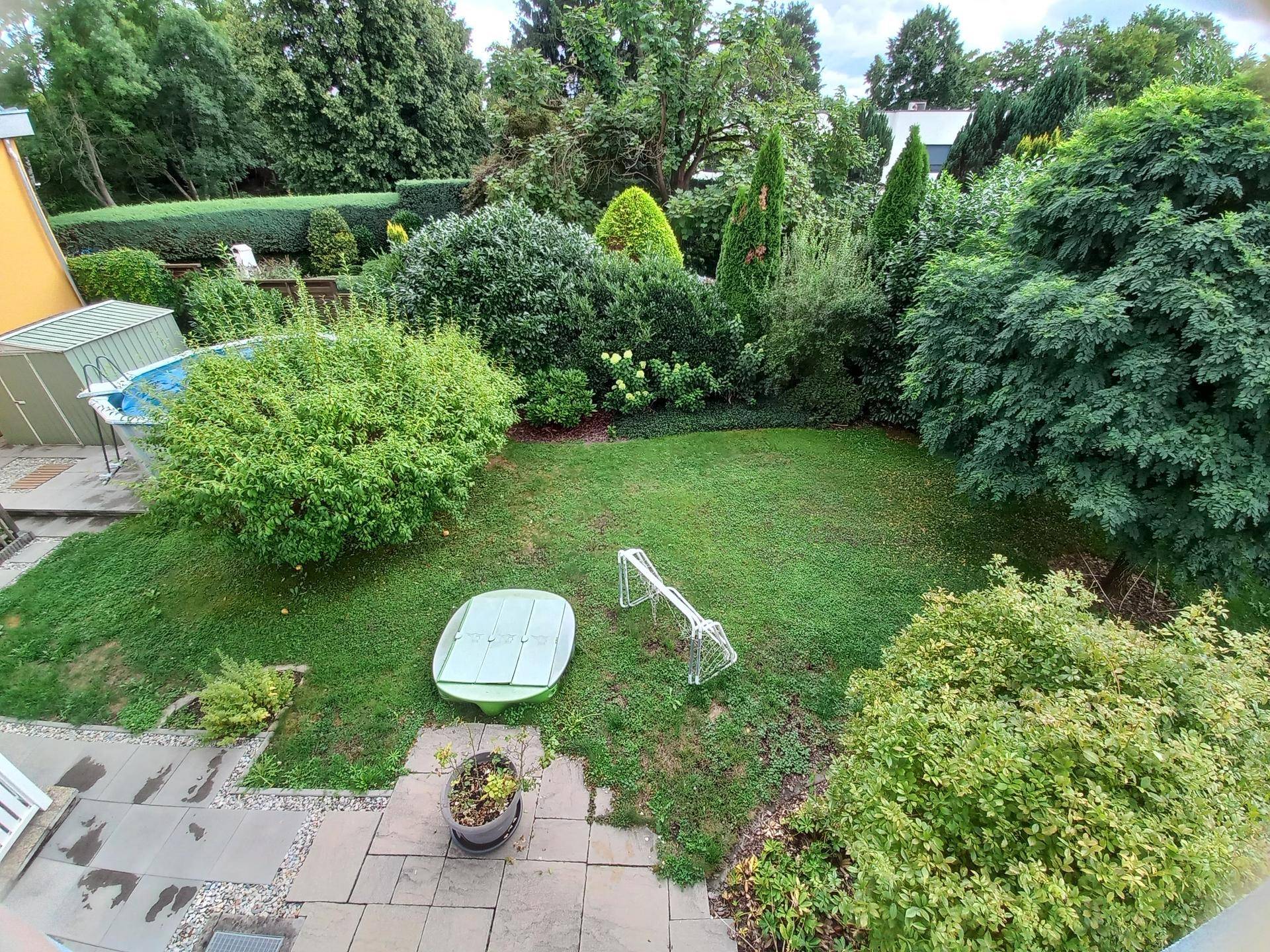 Gepflegter Garten mit Rasenfläche, üppigen Büschen, kleinem Pool und Sitzbereich.