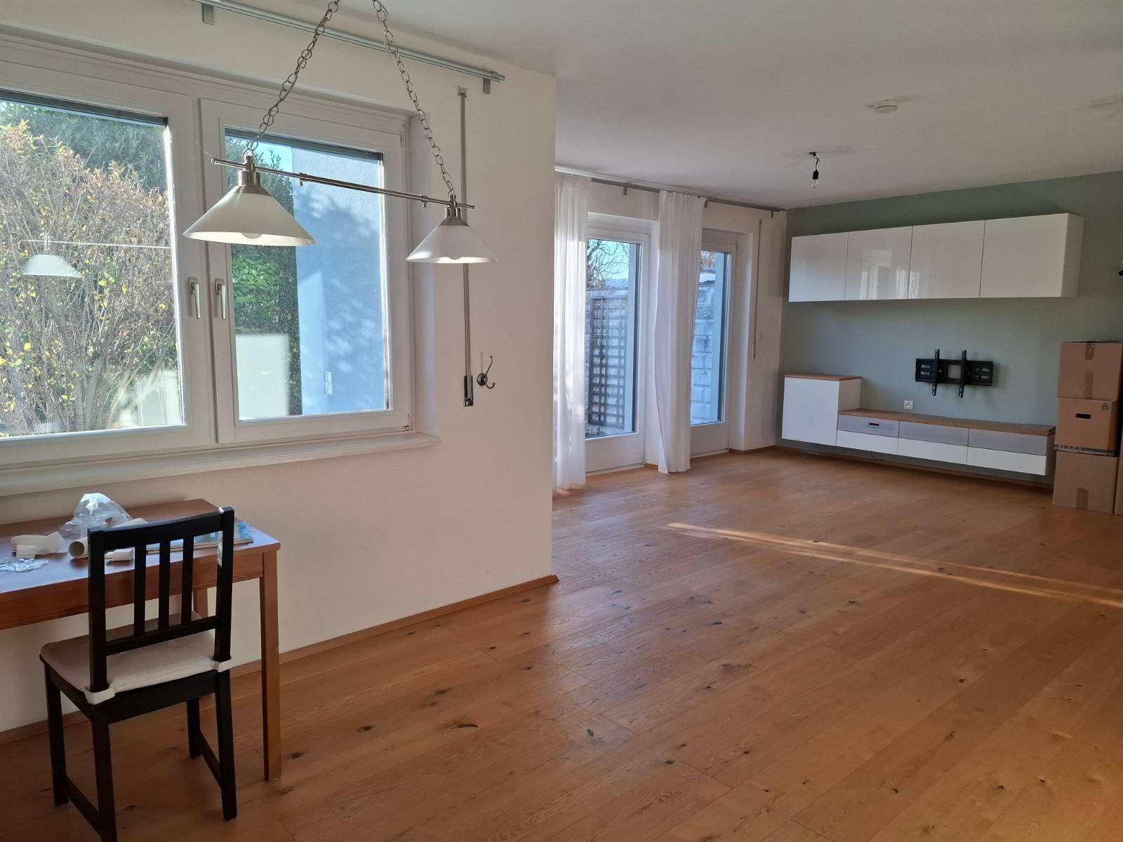 Helles Wohnzimmer mit Holzboden, großen Fenstern und Blick in den Garten.