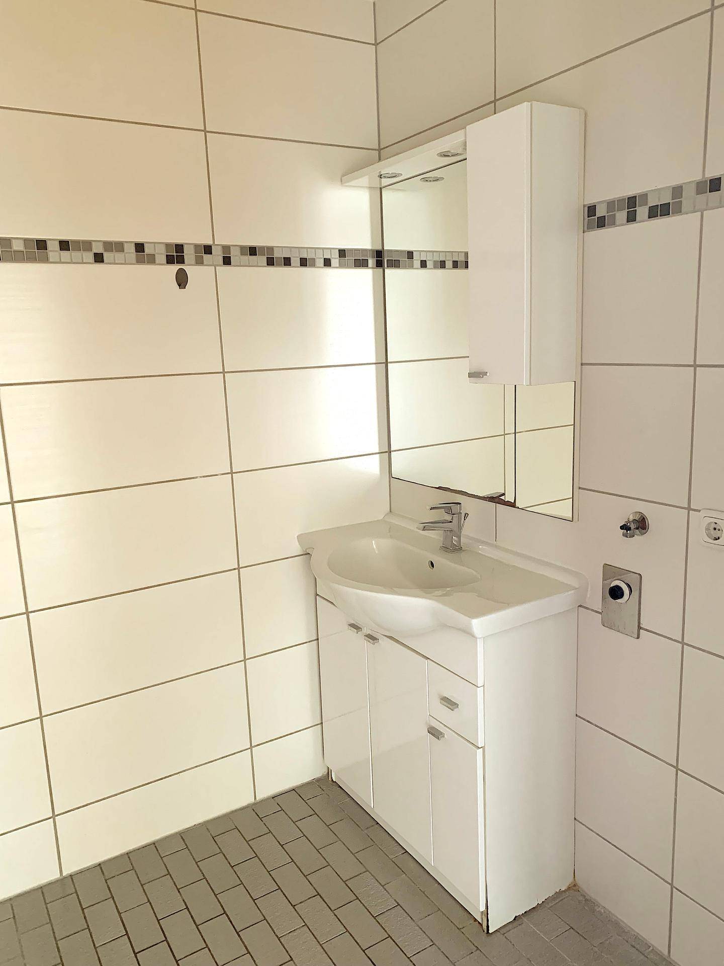 Modernes Badezimmer mit Waschtisch, Spiegelschrank und hellen Wand- und Bodenfliesen.