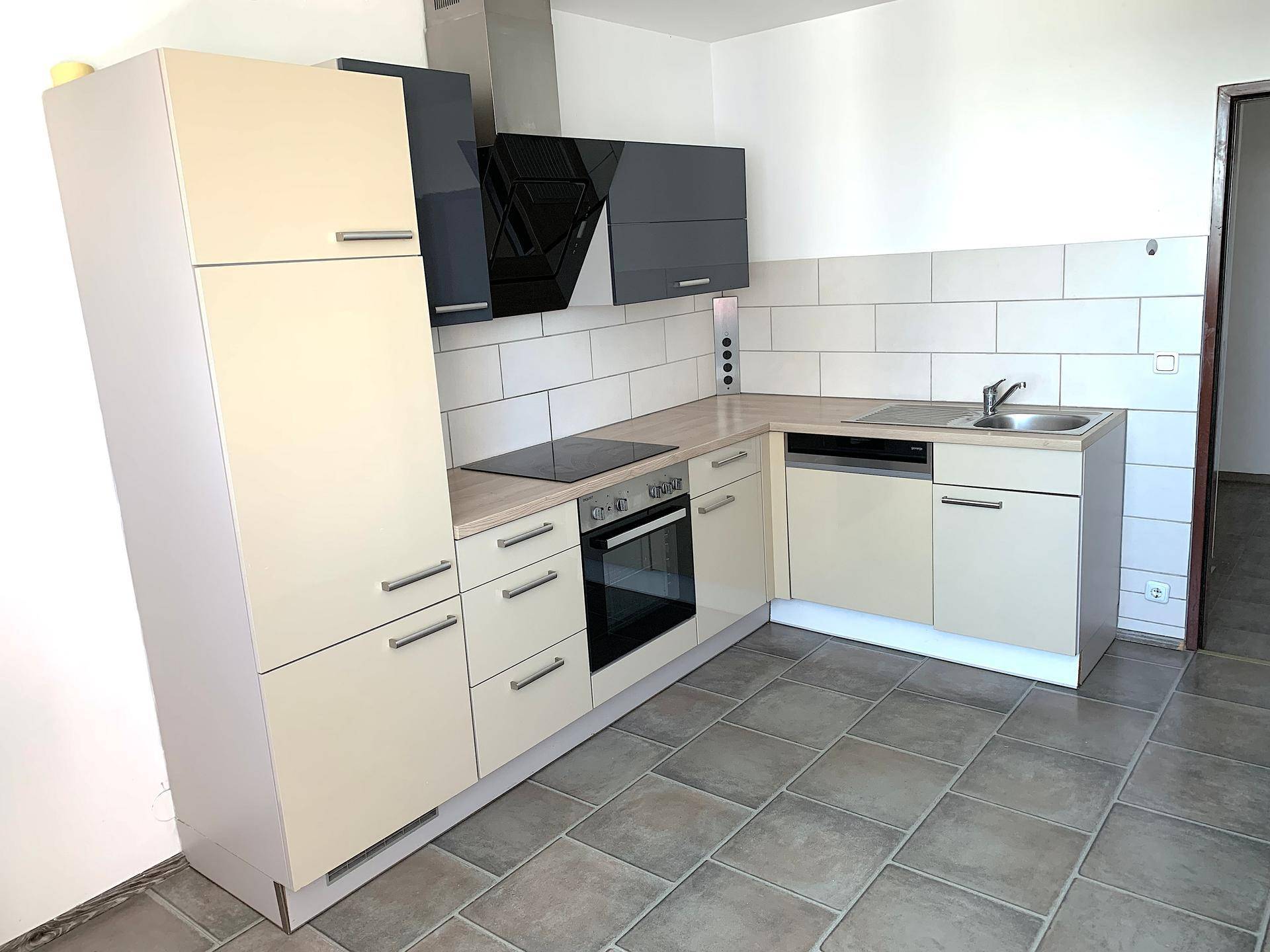 Voll ausgestattete Einbauküche mit beigen und schwarzen Elementen, Herd und Spülmaschine.