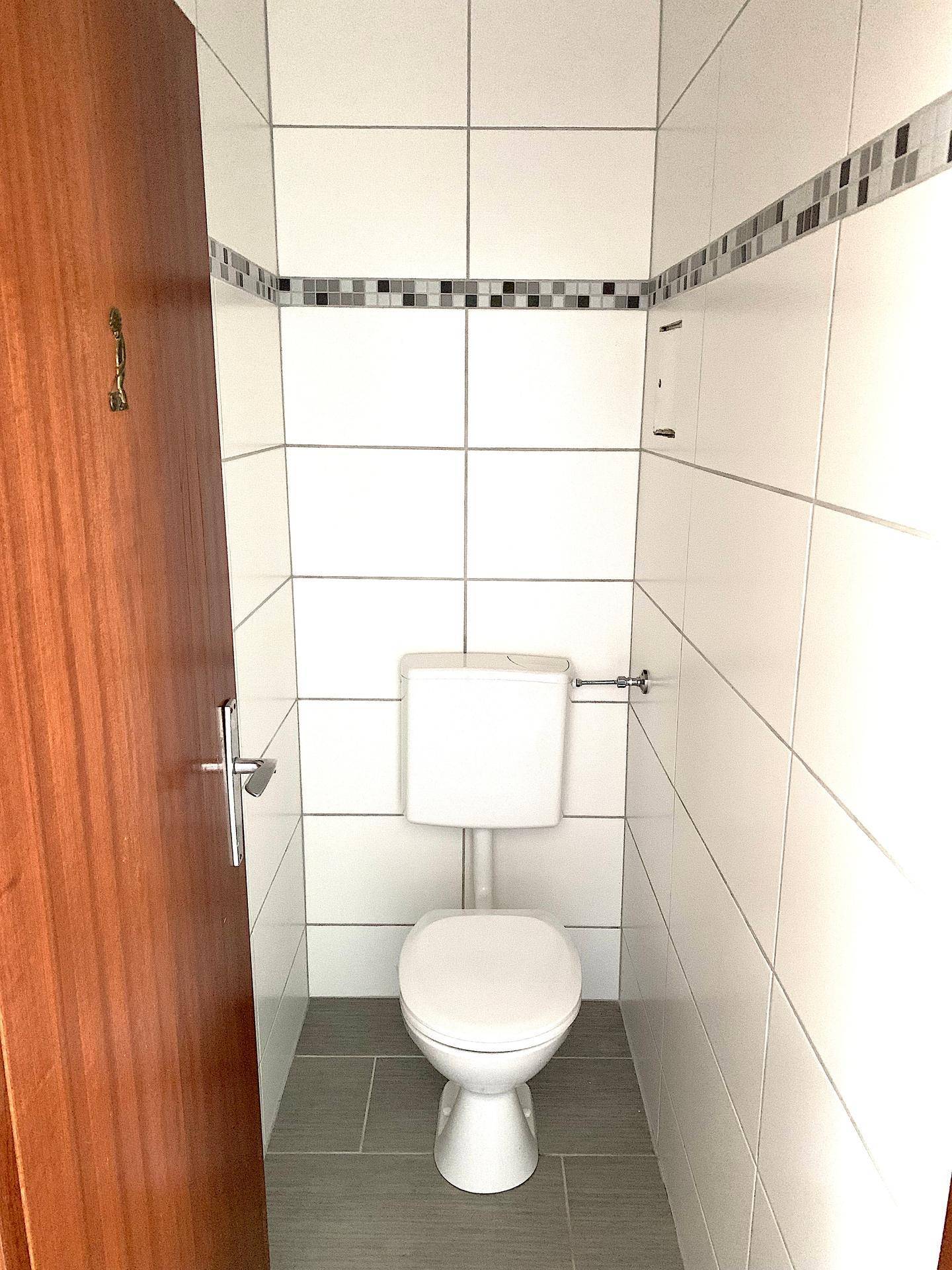 Separates WC mit Toilette und hellen Wand- und Bodenfliesen.