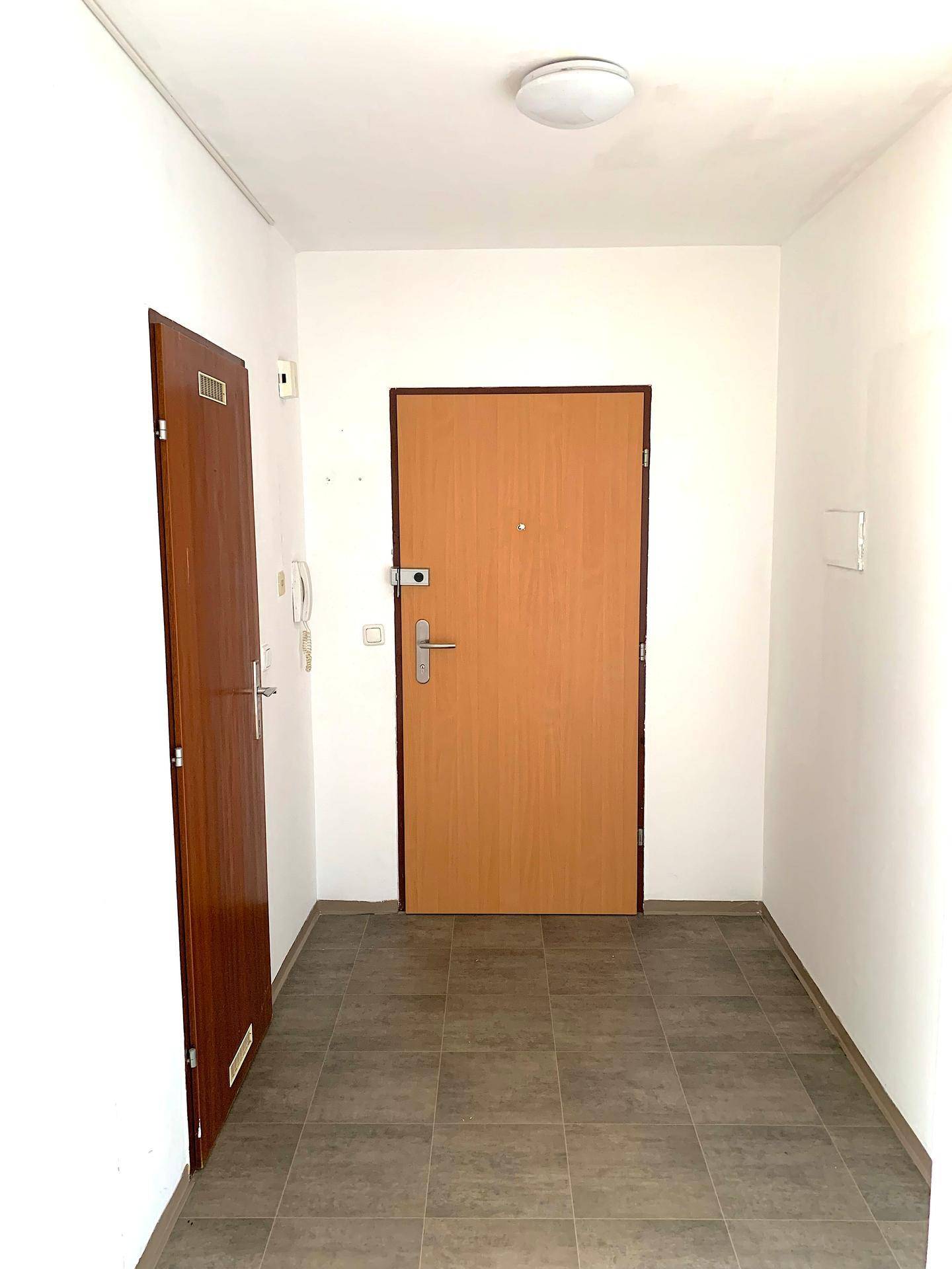 Heller Eingangsbereich mit Fliesenboden und zwei Holztüren.