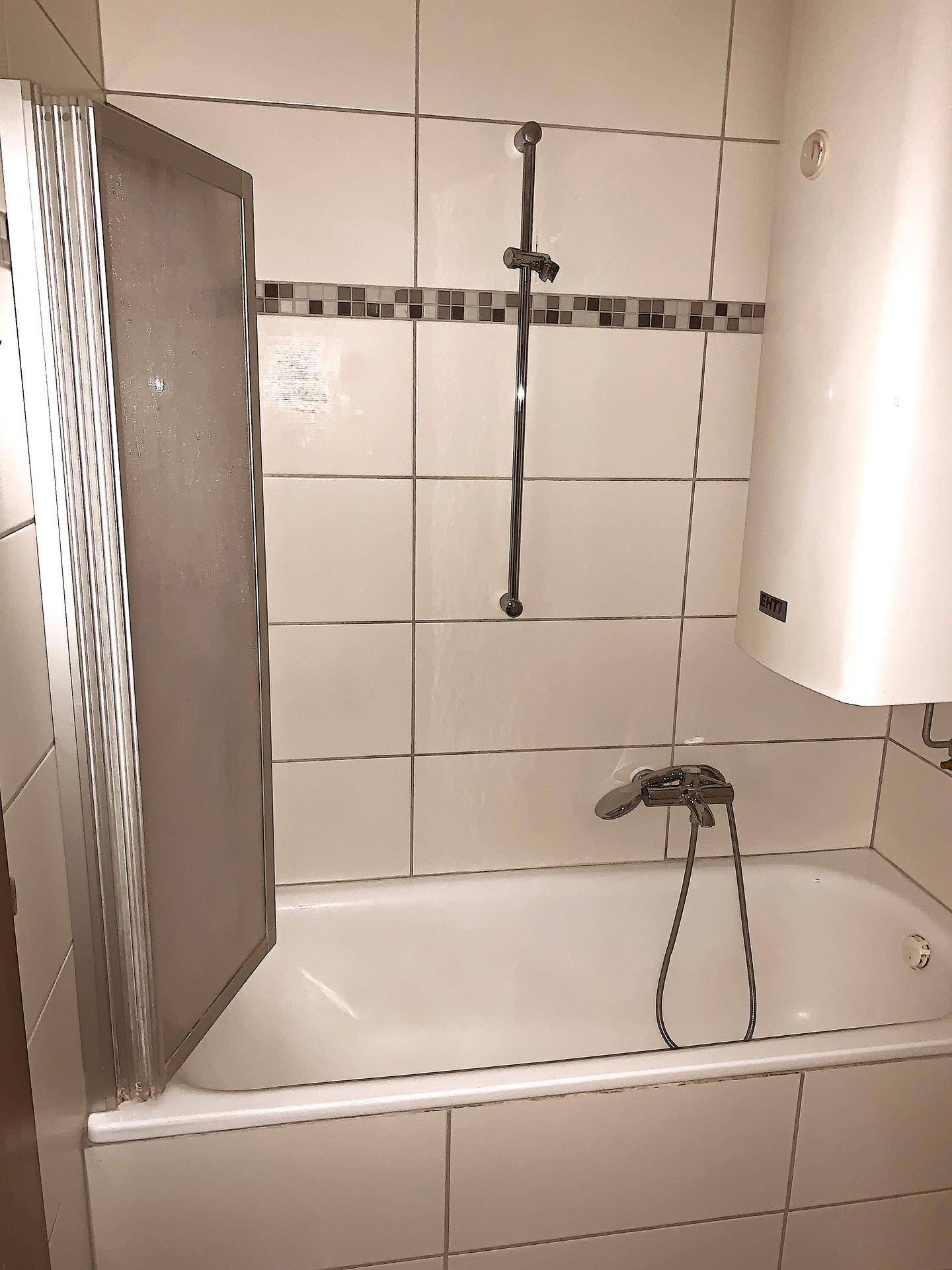 Badezimmer mit Badewanne, Duschvorrichtung und weißen Wandfliesen.