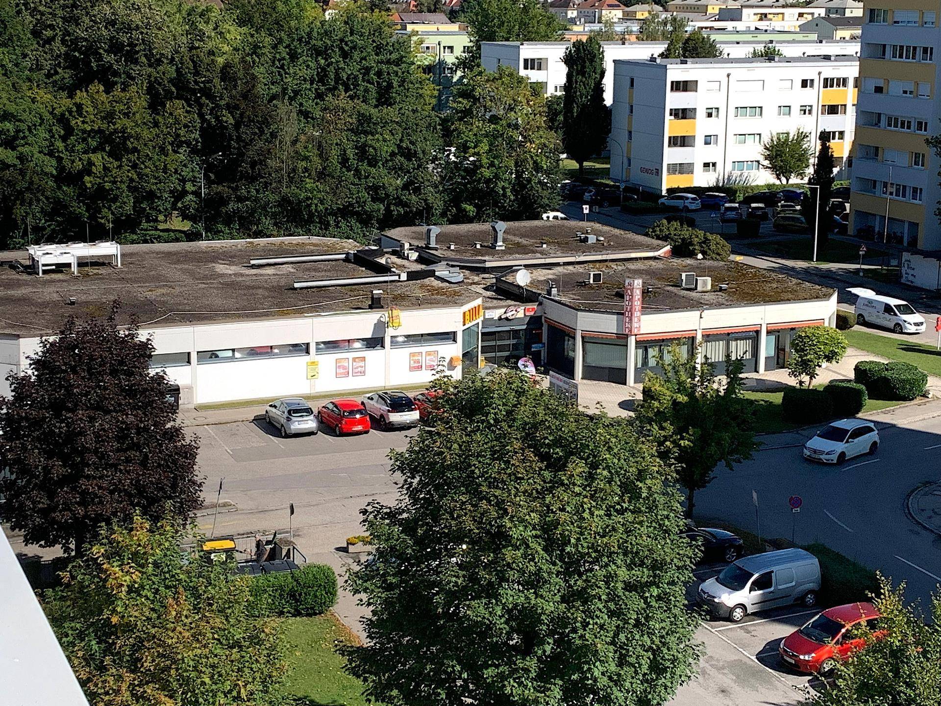 Luftaufnahme von Geschäftsgebäuden, einem Parkplatz und umliegenden Bäumen.