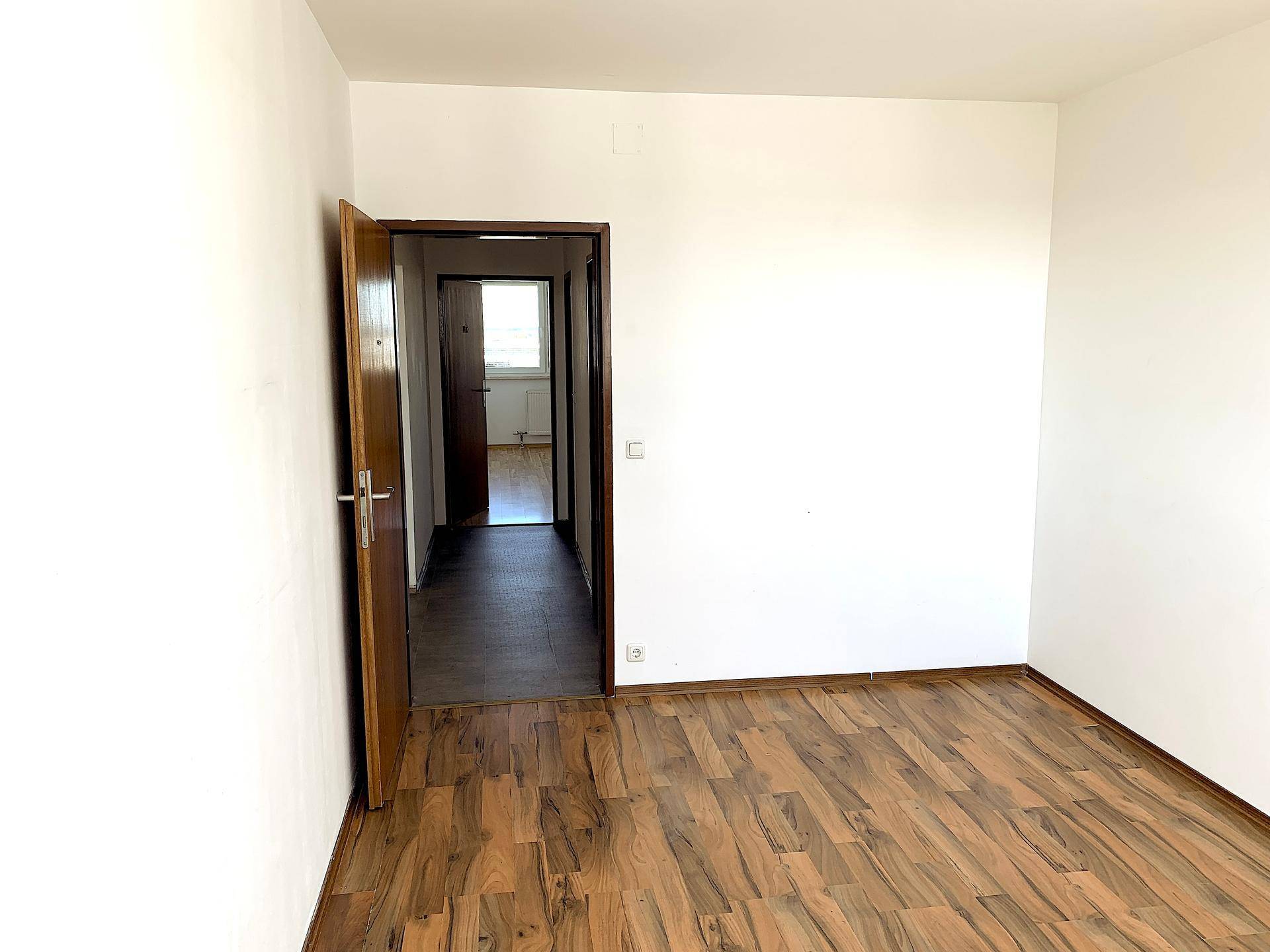 Leeres Zimmer mit Laminatboden und offener Tür zu einem weiteren Raum.
