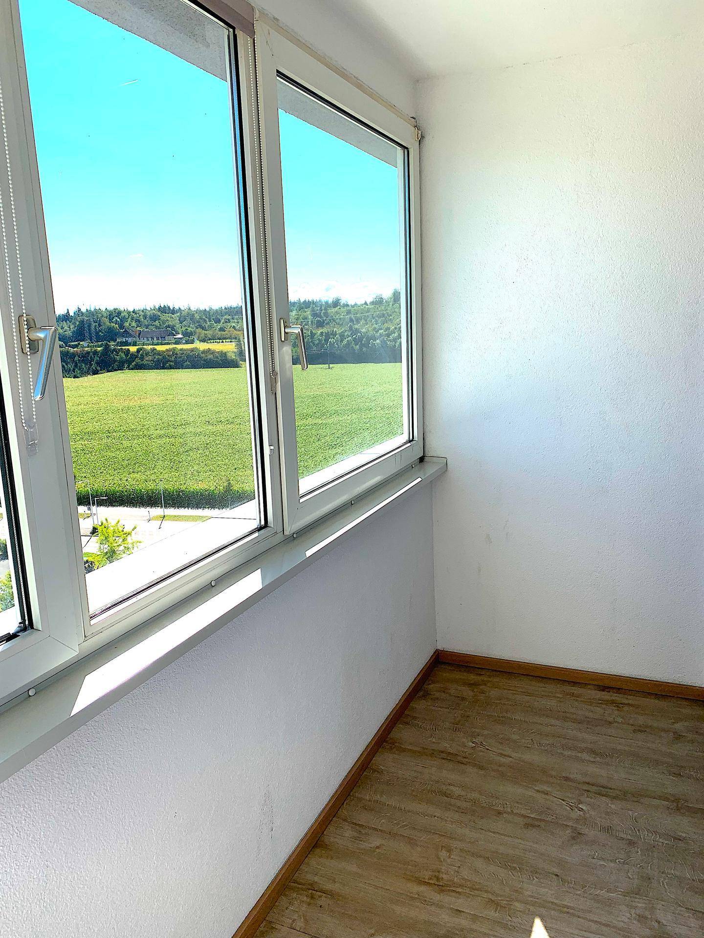 Kleiner, heller Raum mit Fenster und Blick auf grüne Felder.