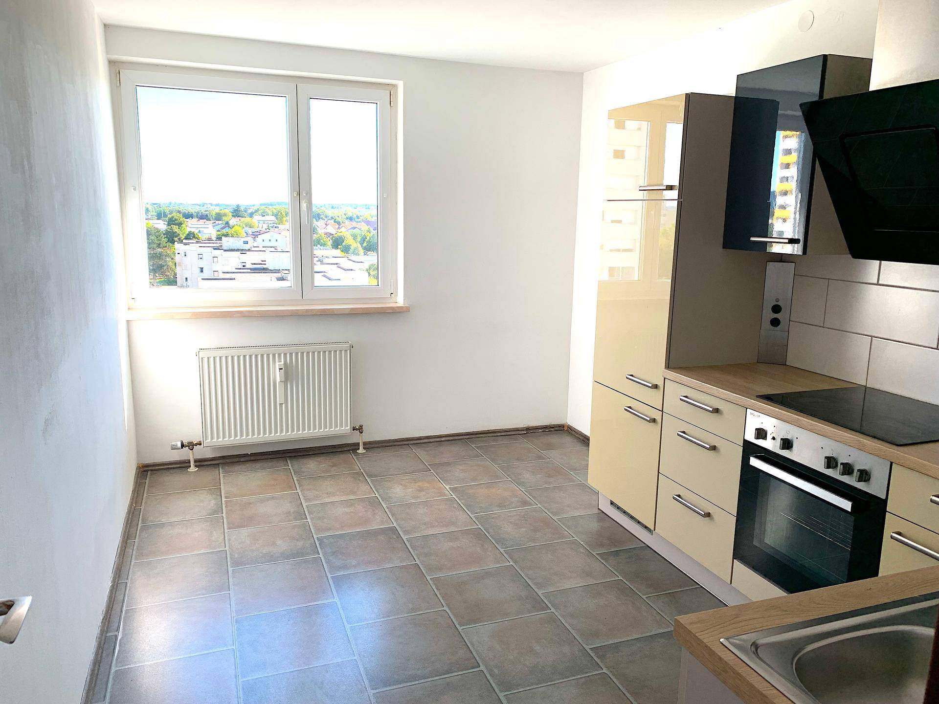 Moderne Einbauküche mit beigen Schränken, Fliesenboden und Fenster mit Ausblick.