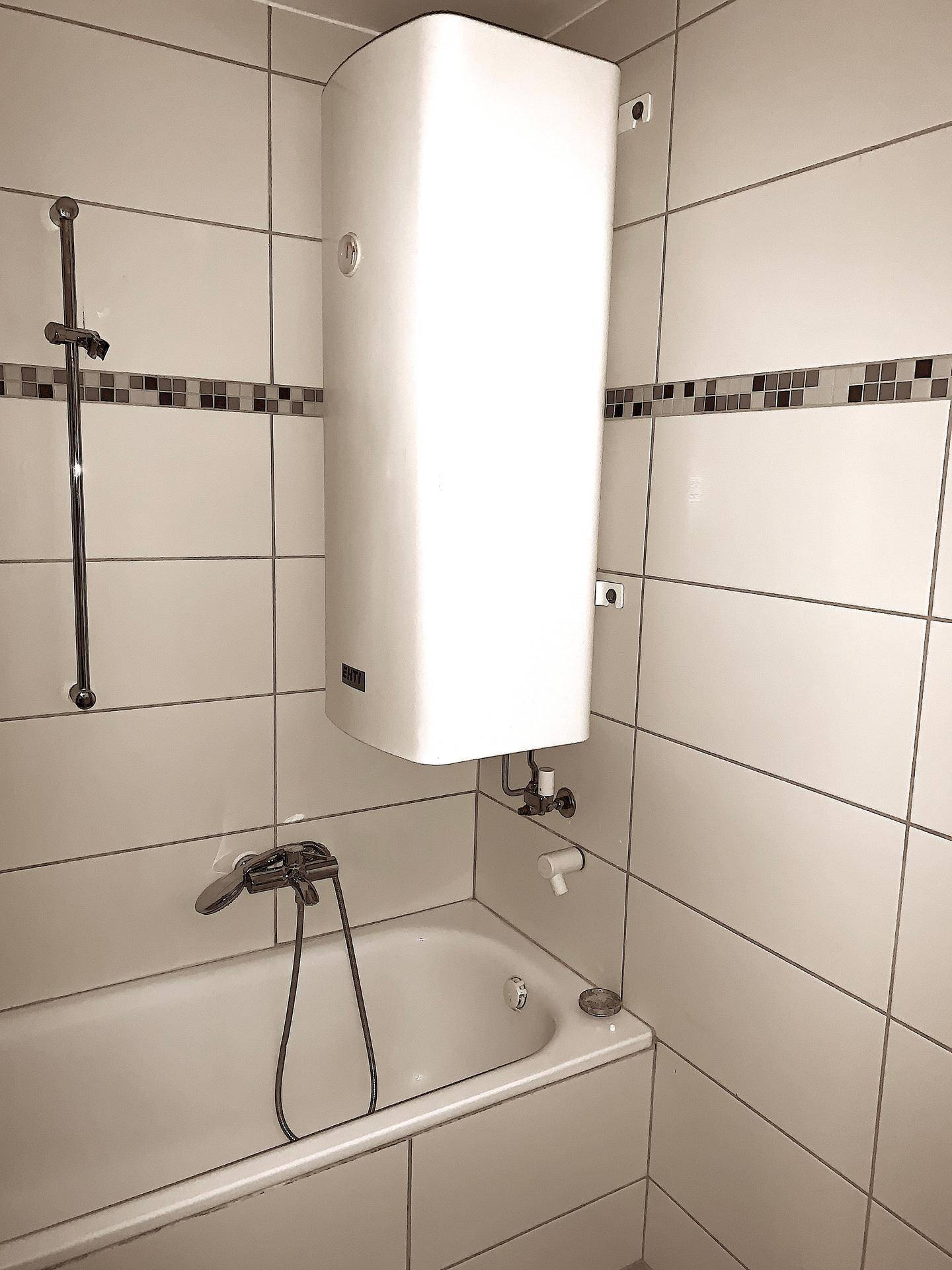 Badezimmer mit Badewanne, Duschvorrichtung und einem Warmwasserboiler.