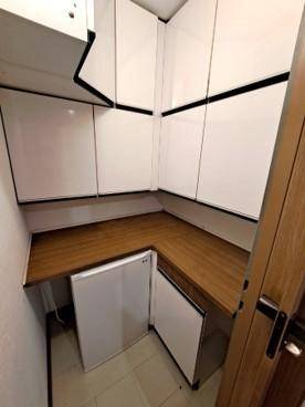 Kleiner Hauswirtschaftsraum mit weißen Schränken, Arbeitsplatte aus Holz und integrierten Geräten.