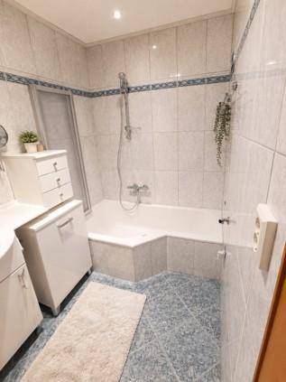 Badezimmer mit Eckbadewanne, Duschvorrichtung und hellen Fliesen an Wänden und Boden.