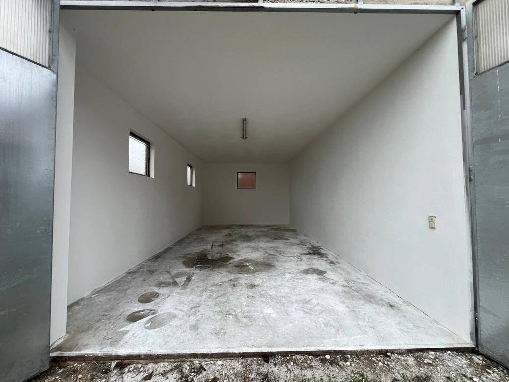 Geräumige Garage mit geöffneten Toren, Betonboden und kleinen Seitenfenstern für Licht.