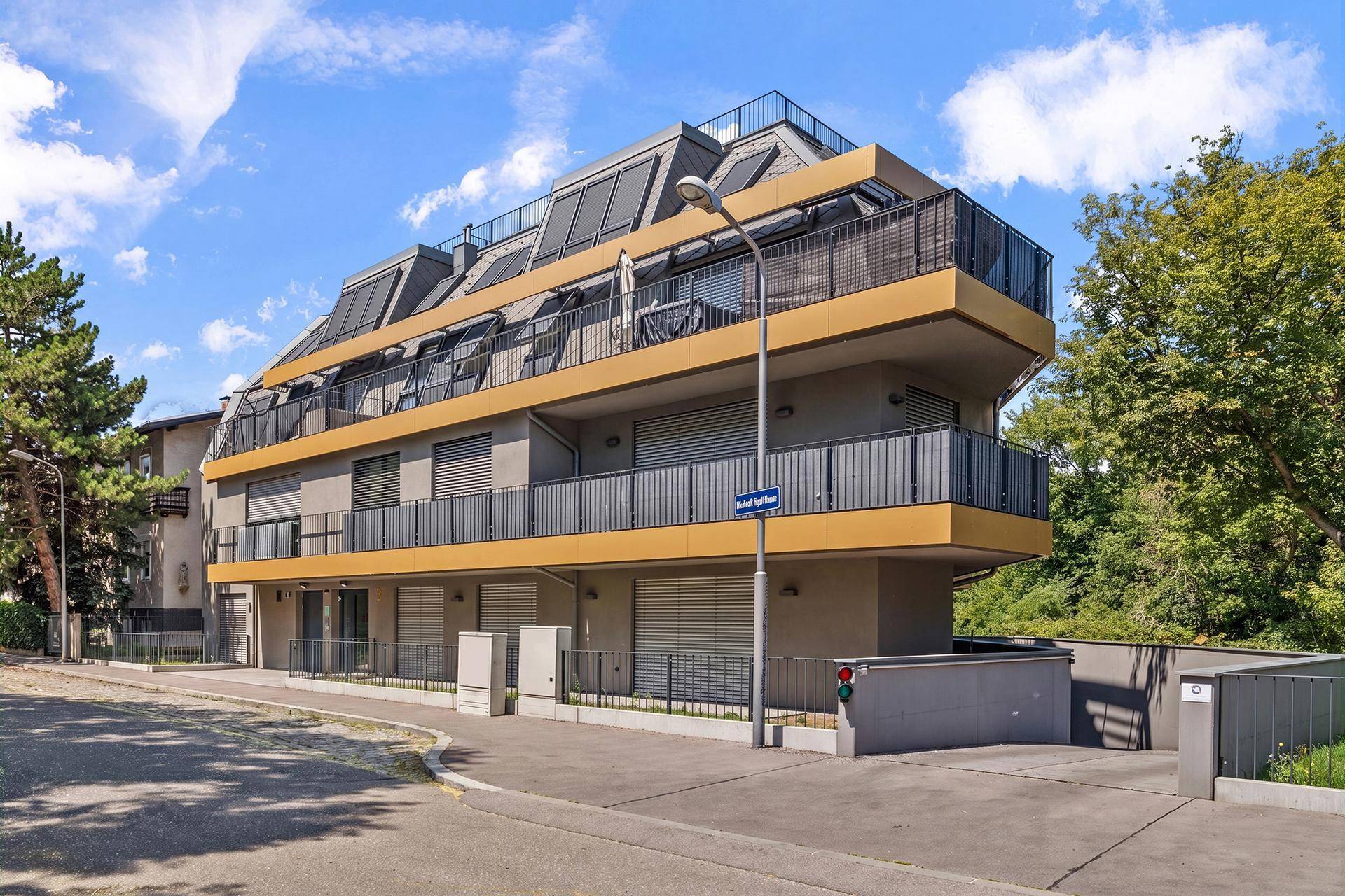 Moderne Wohnanlage mit mehreren Balkonen und Dachschrägen in städtischer Umgebung.