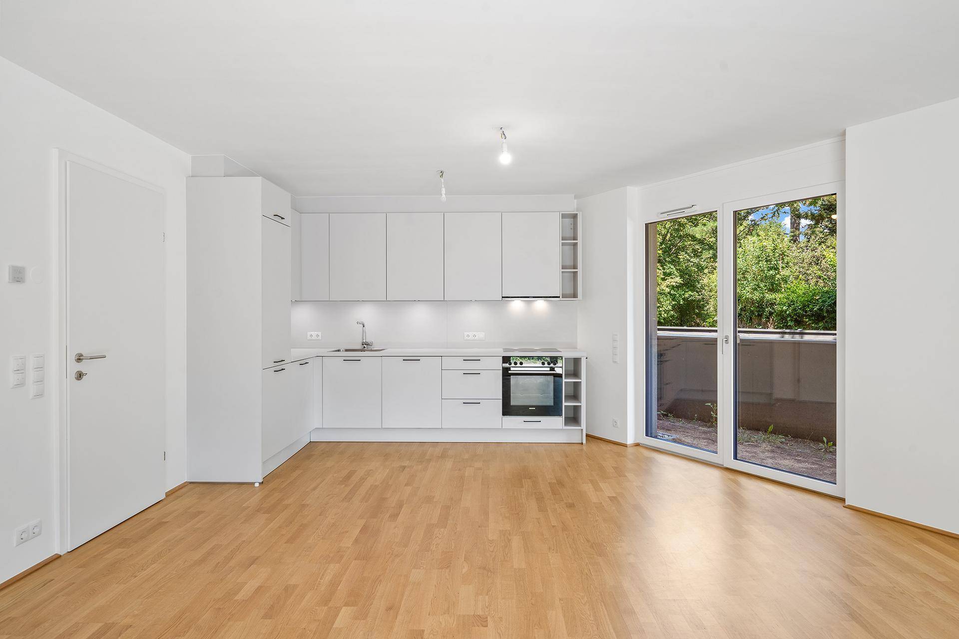 Moderne, helle Einbauküche mit weißen Schränken und integriertem Backofen, offen zum Wohnbereich.