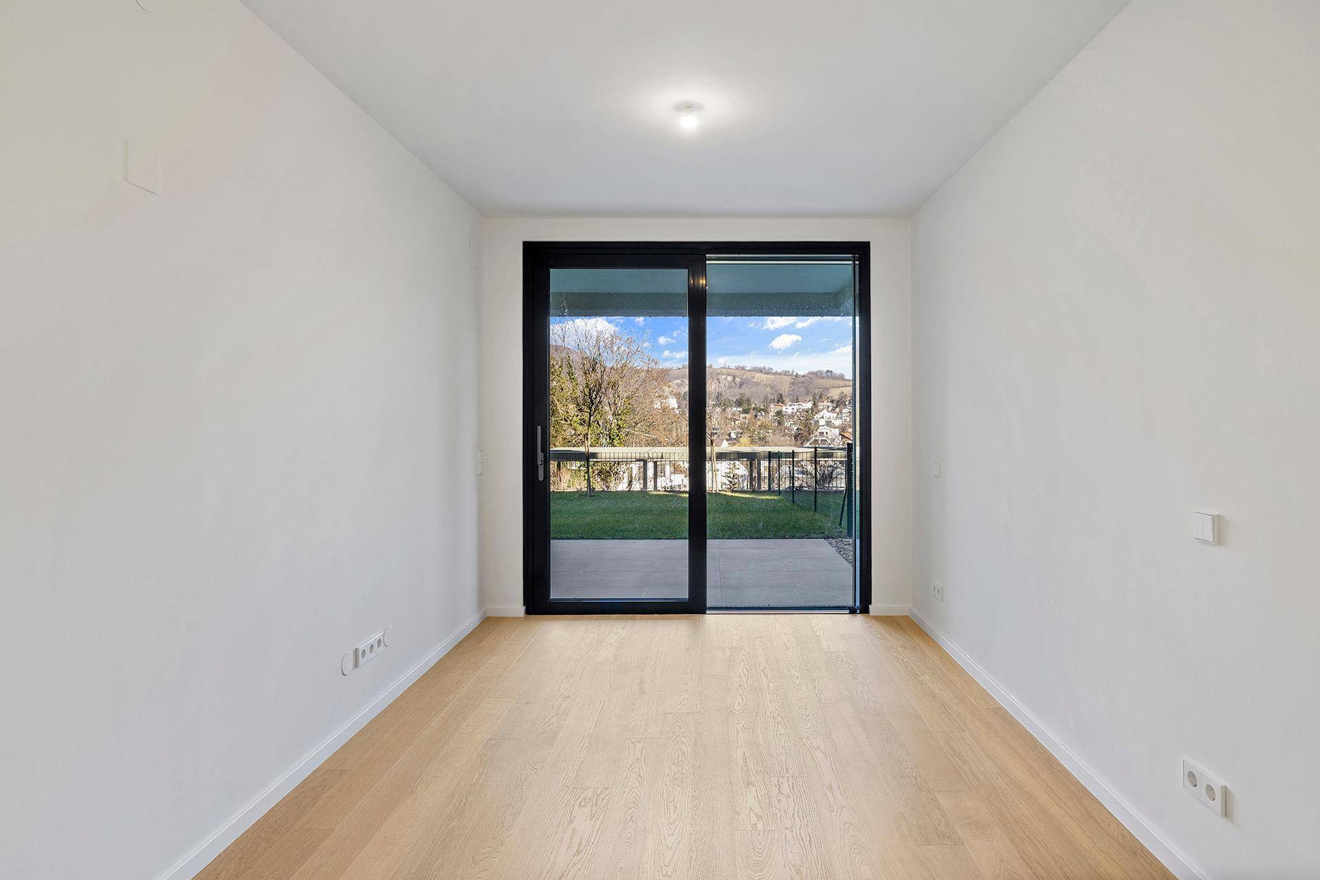 Lichtdurchflutetes Zimmer mit Holzboden und direktem Zugang zum Garten durch eine große Glasschiebetür.