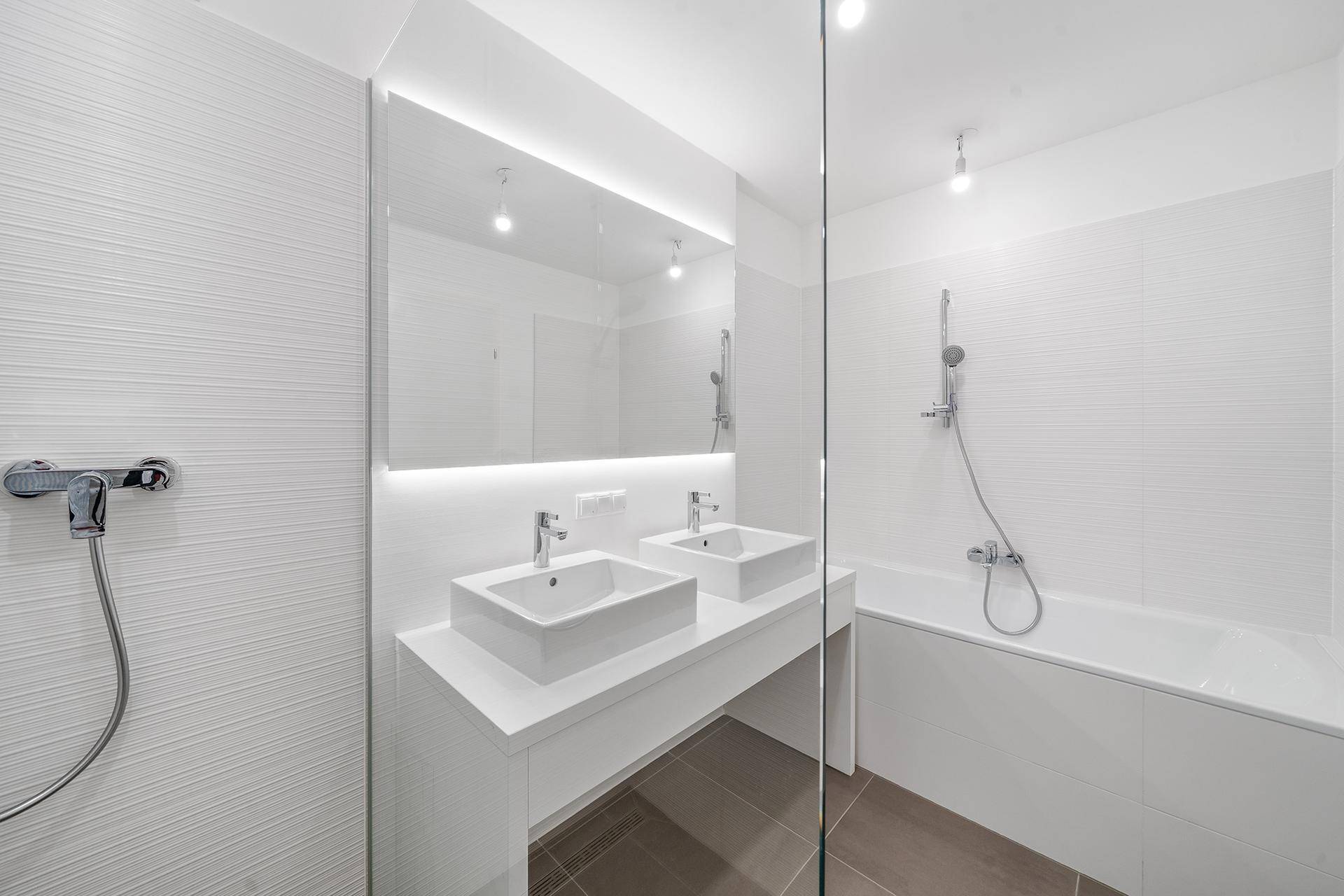 Modernes Badezimmer mit Doppelwaschbecken, Badewanne und separater Dusche, hell gefliest.