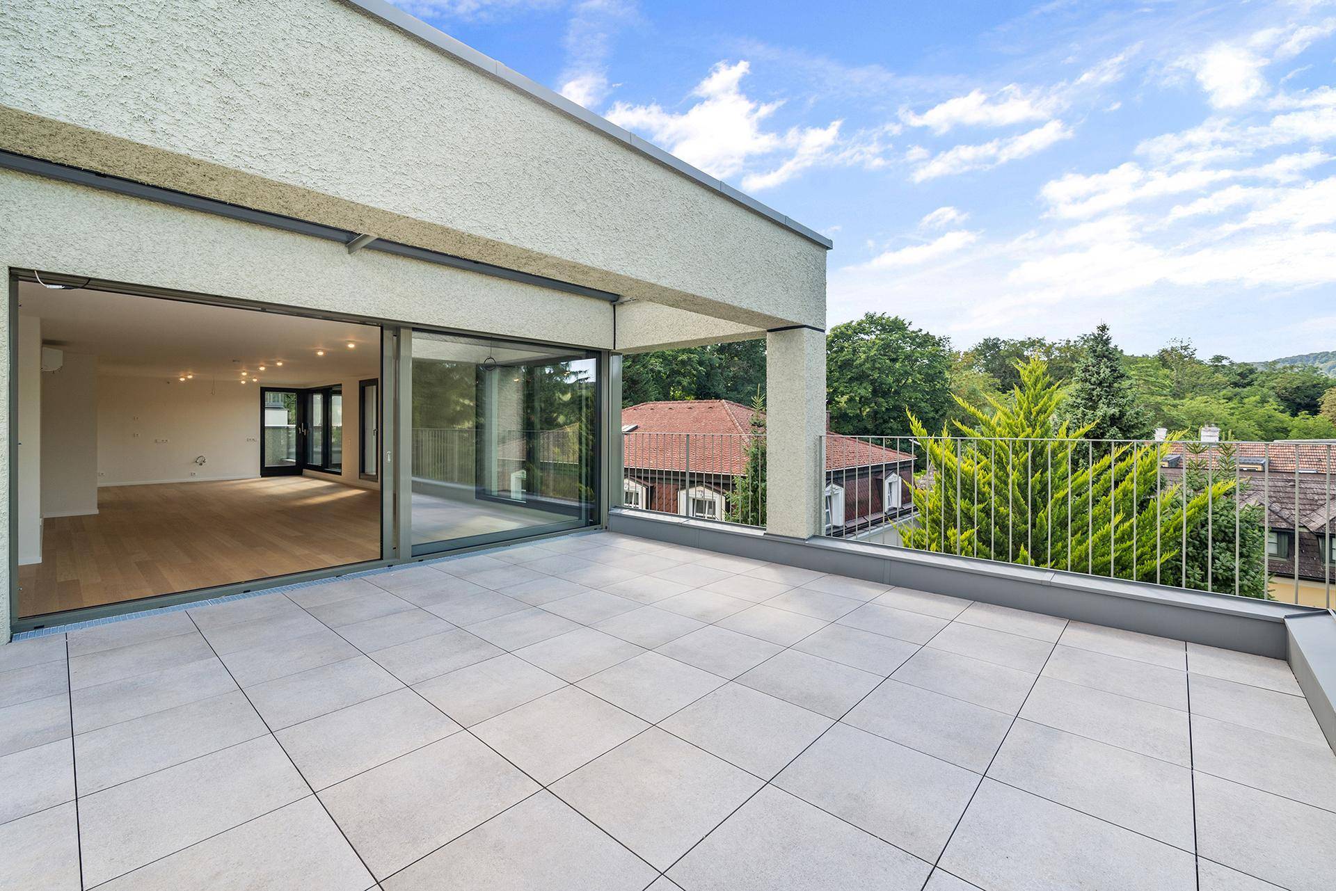 Helle Terrasse mit Fliesenboden und Blick auf die umliegende Natur und die Dächer der Häuser.