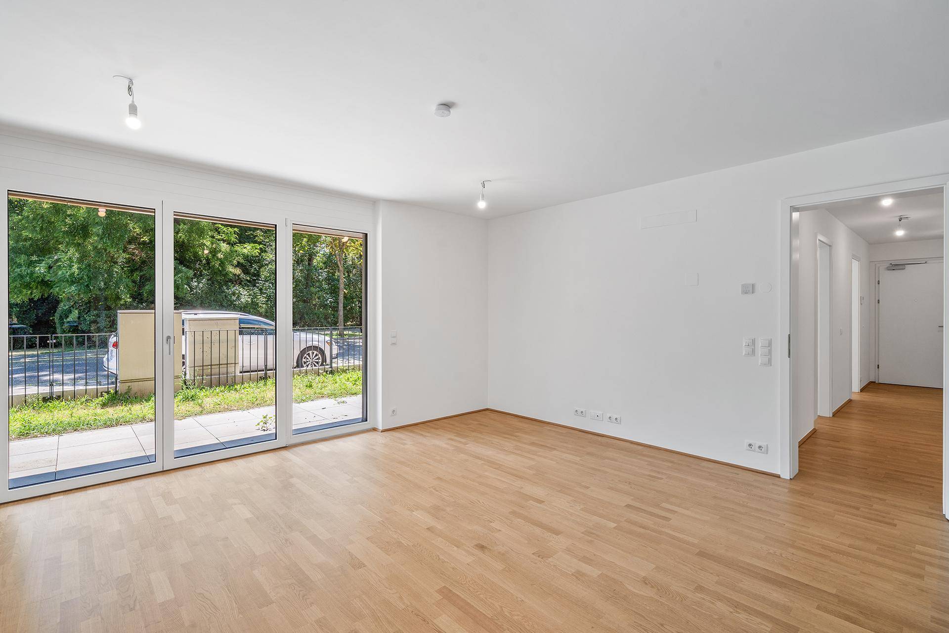 Geräumiges, helles Wohnzimmer mit Parkettboden und großen Fenstern zum Balkon.
