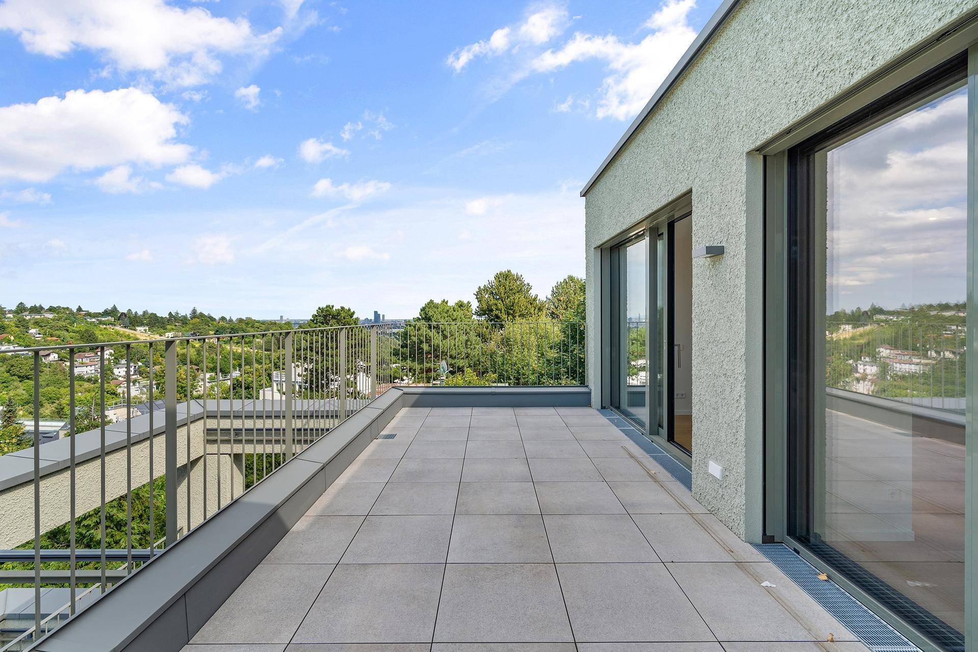 Lange, moderne Terrasse mit Fliesenboden und Geländer, bietet einen weiten Blick über die Umgebung.