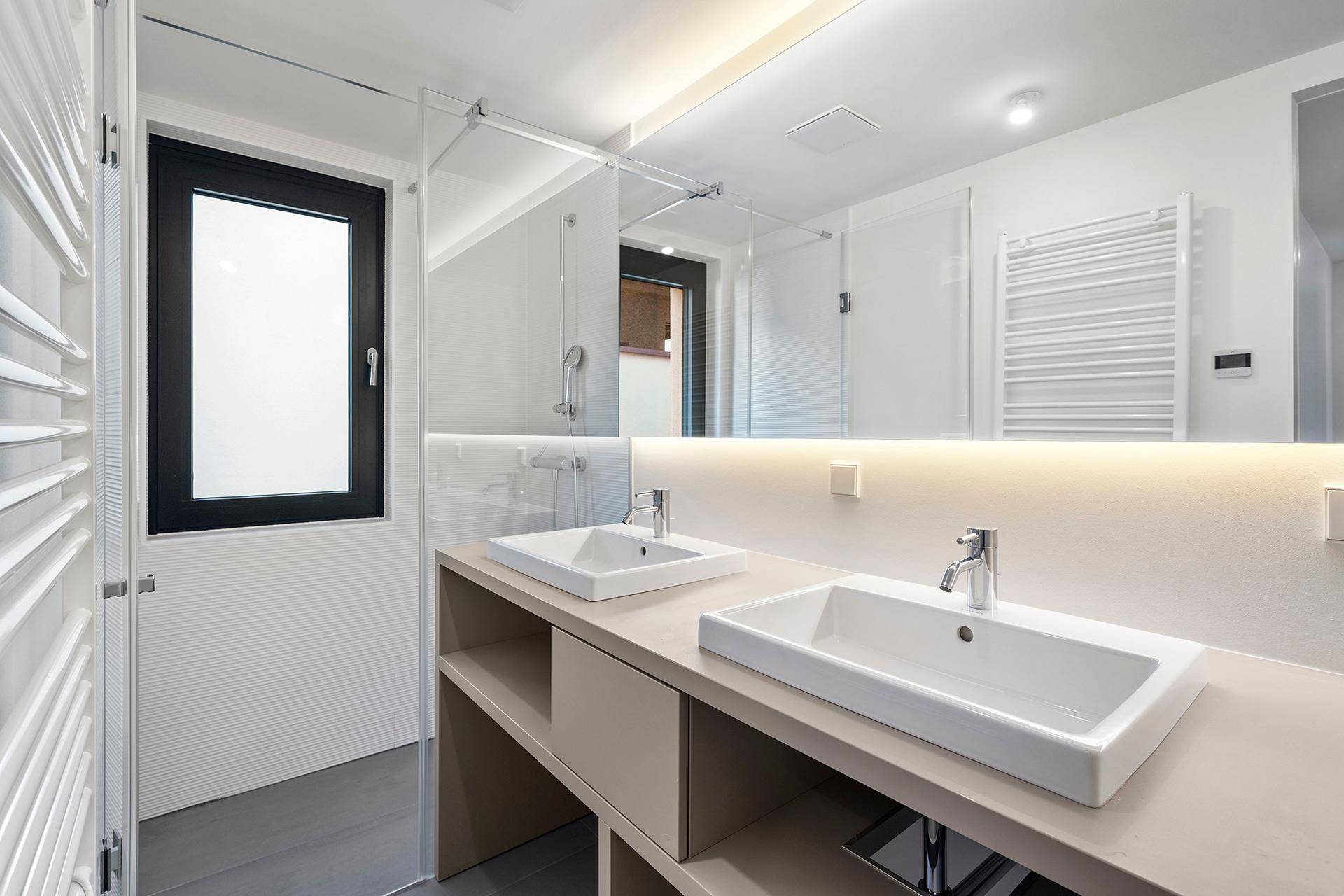 Modernes Badezimmer mit Doppelwaschbecken, großem Spiegel und beheiztem Handtuchhalter.