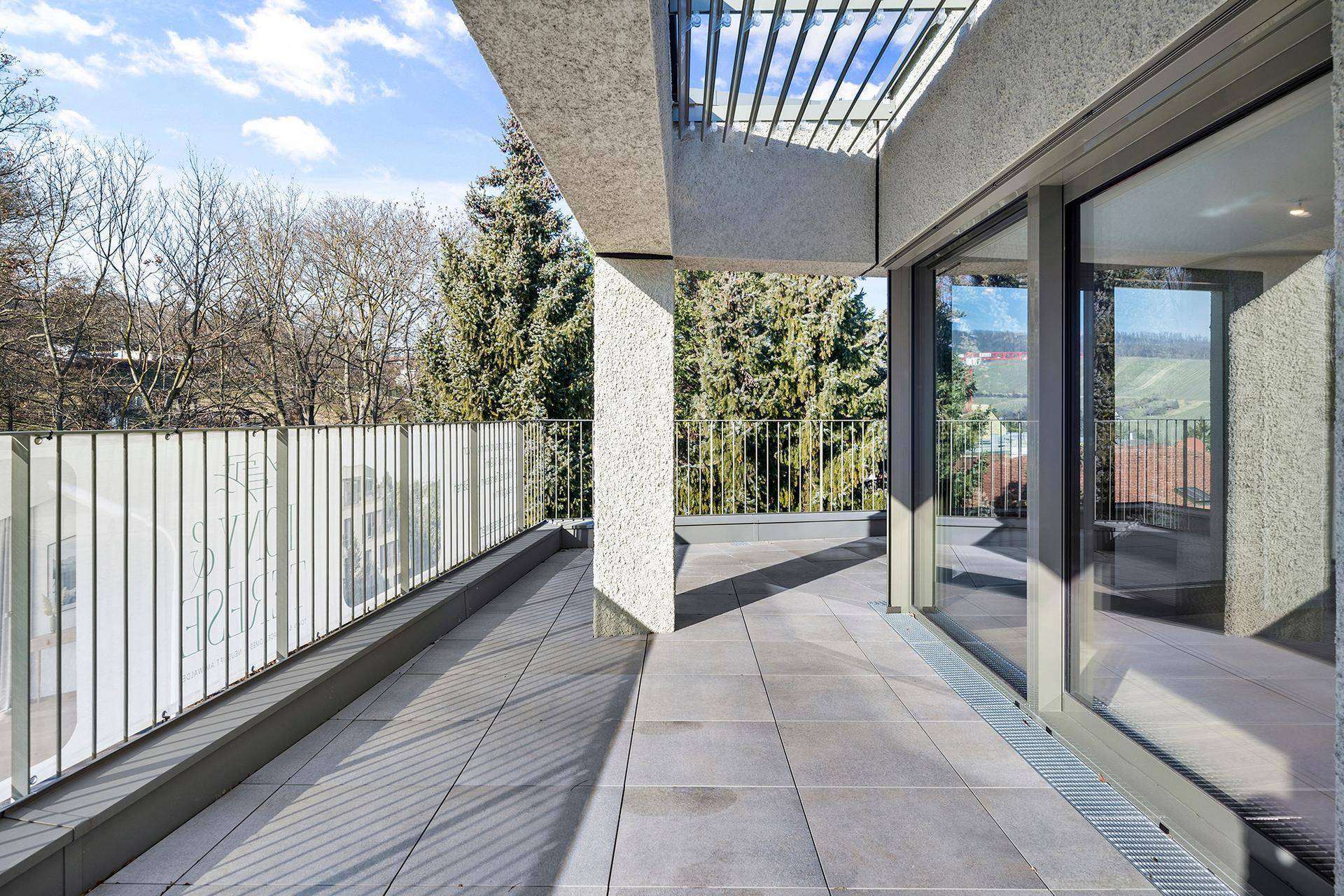 Moderne Terrasse mit großen Glasfronten und Blick auf die umliegende Natur und Weinberge.