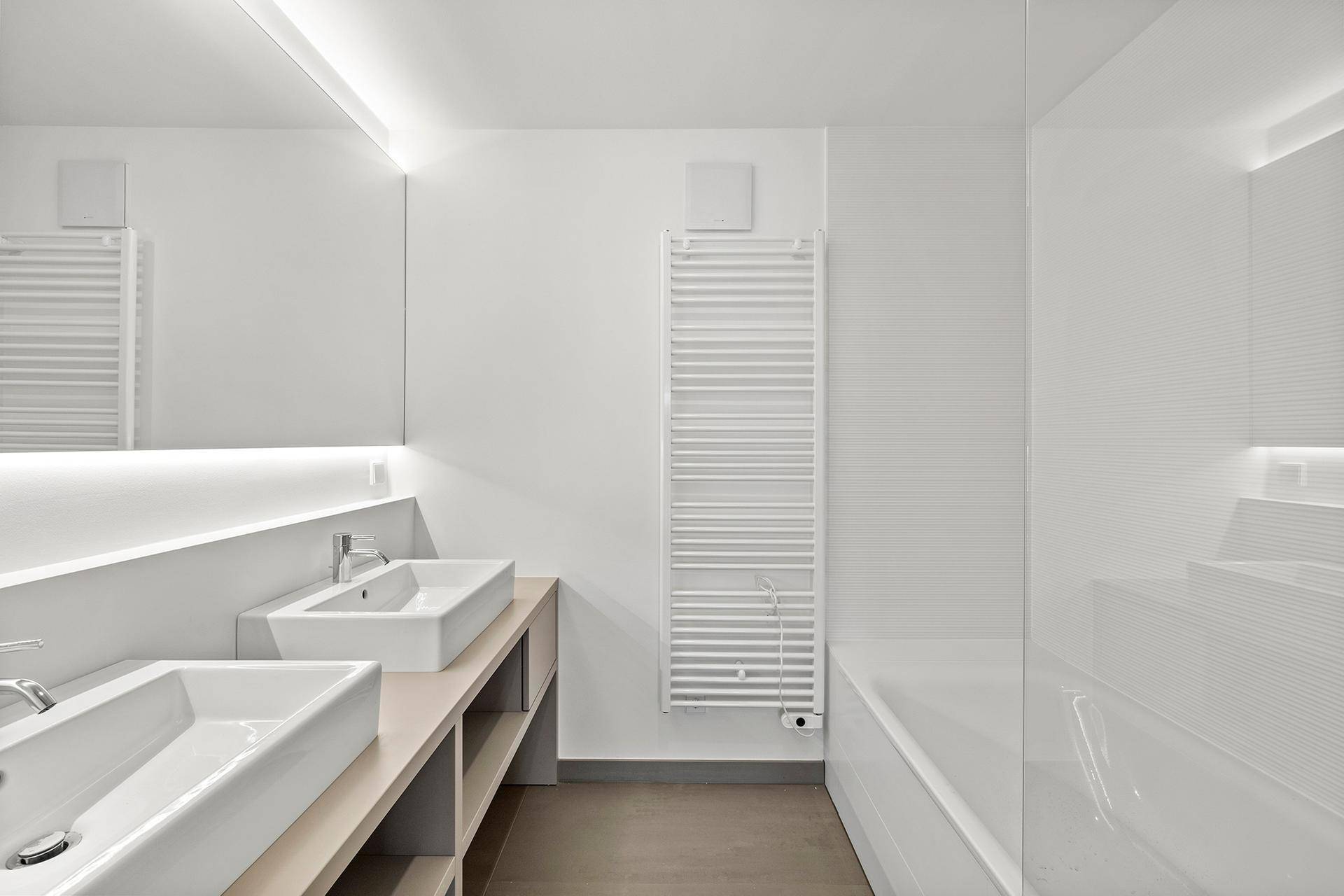 Modernes Badezimmer mit Doppelwaschbecken, Badewanne und beheiztem Handtuchhalter in minimalistischem Design.